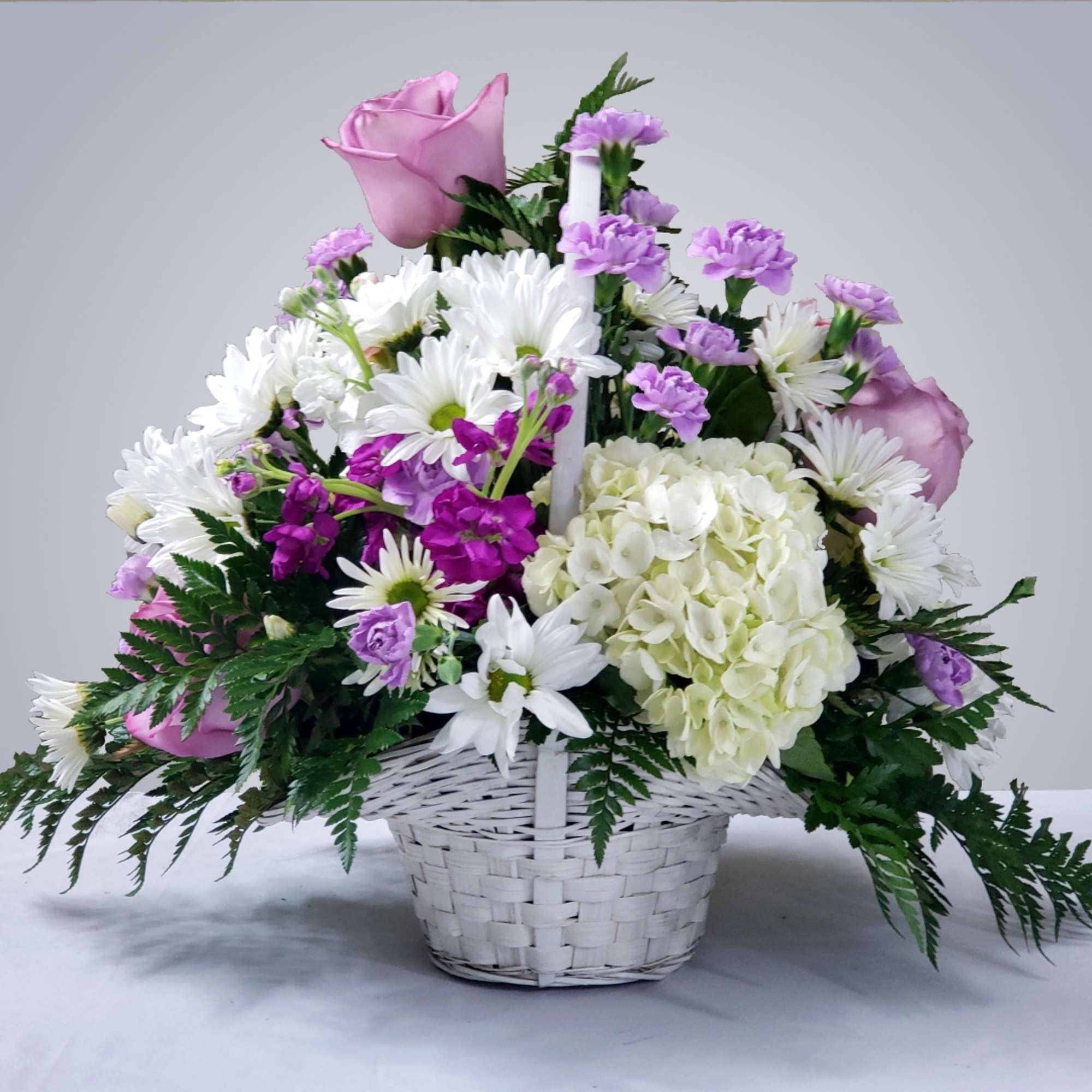 Pink roses, white daisies, and purple flowers in a white basket