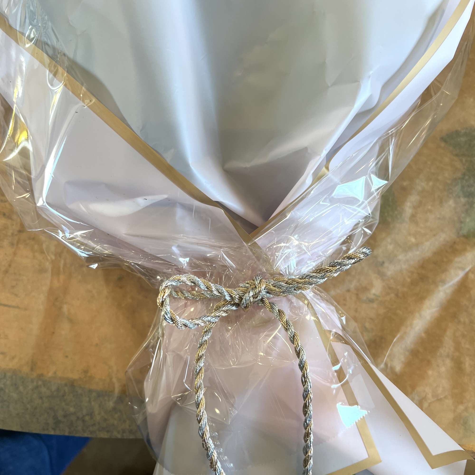 Wrapped bouquet with white paper and gold trim tied with a braided cord