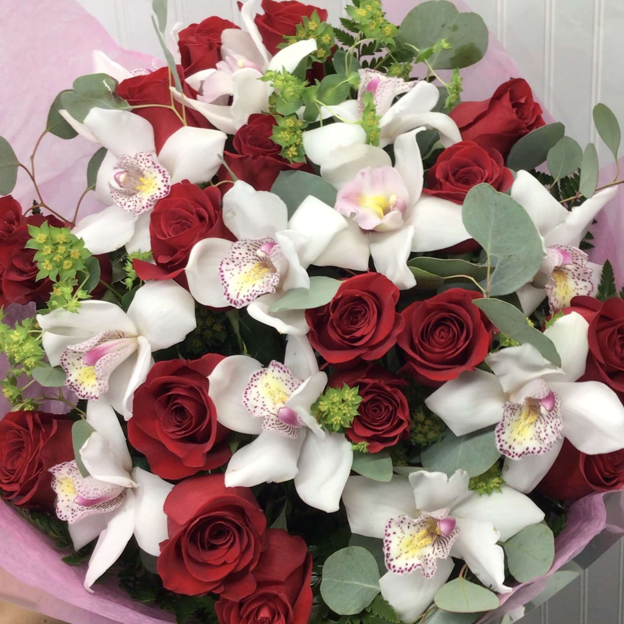 Hand-tied bouquet of red roses and white orchids wrapped in pink paper