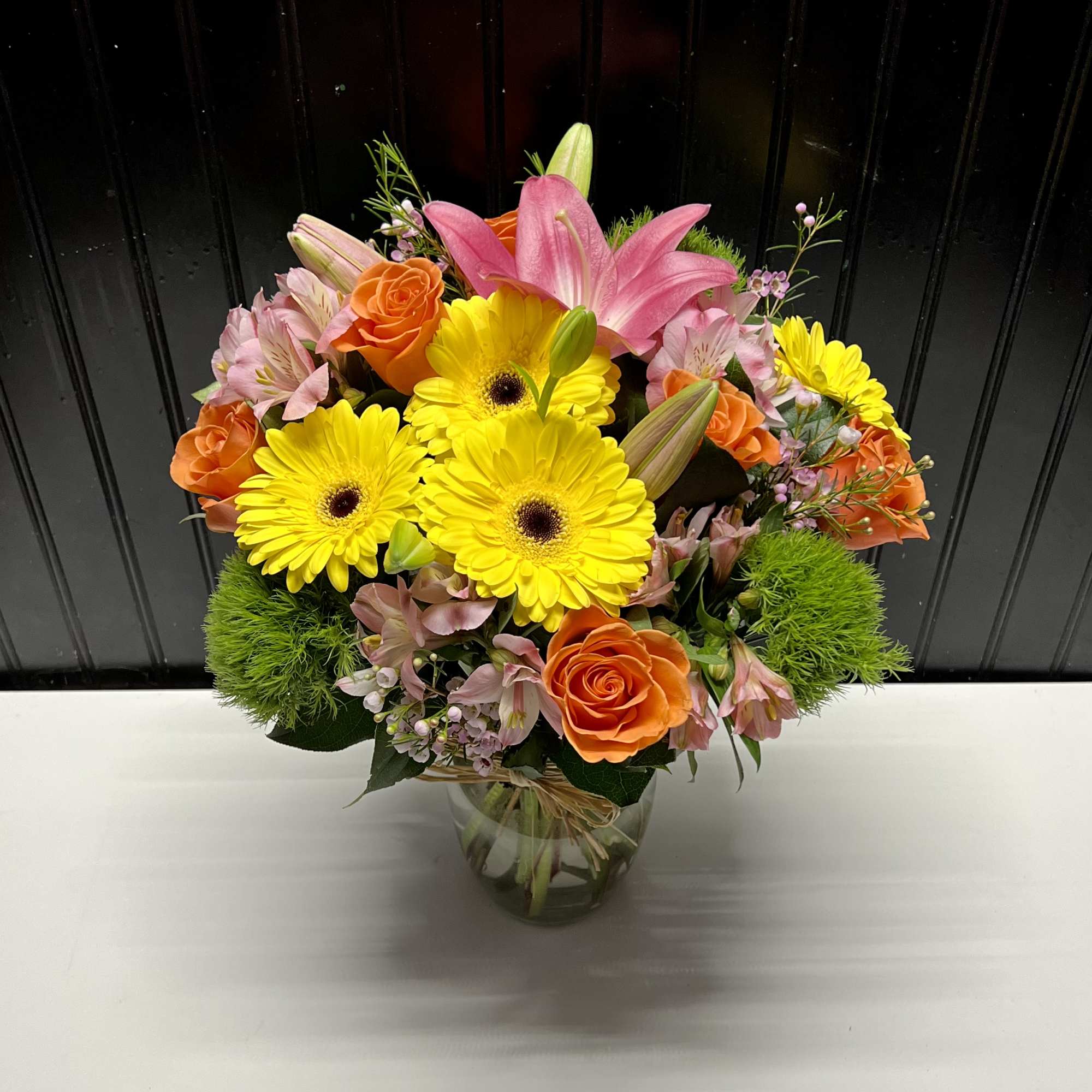 Bouquet of yellow gerbera daisies, pink lilies, and orange roses in a glass vase