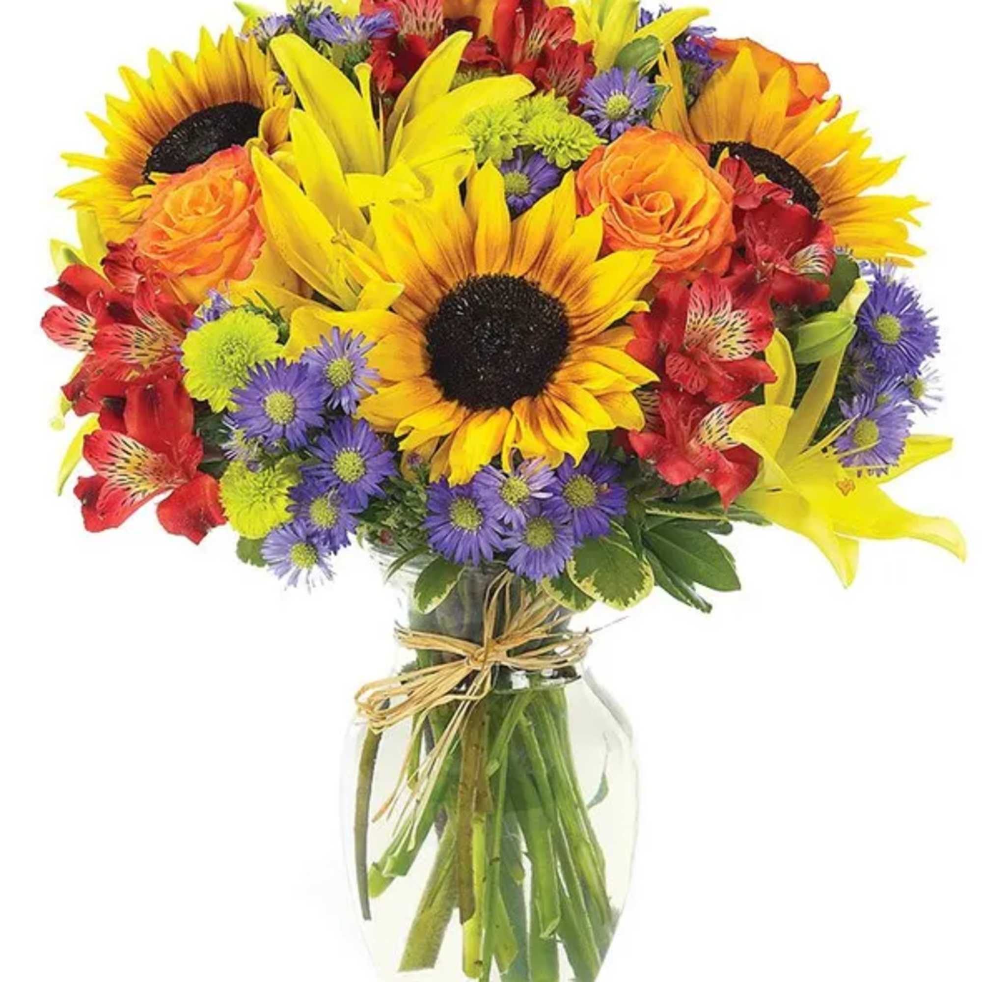 Bright mixed bouquet of sunflowers, roses, lilies, and purple daisies in a glass vase