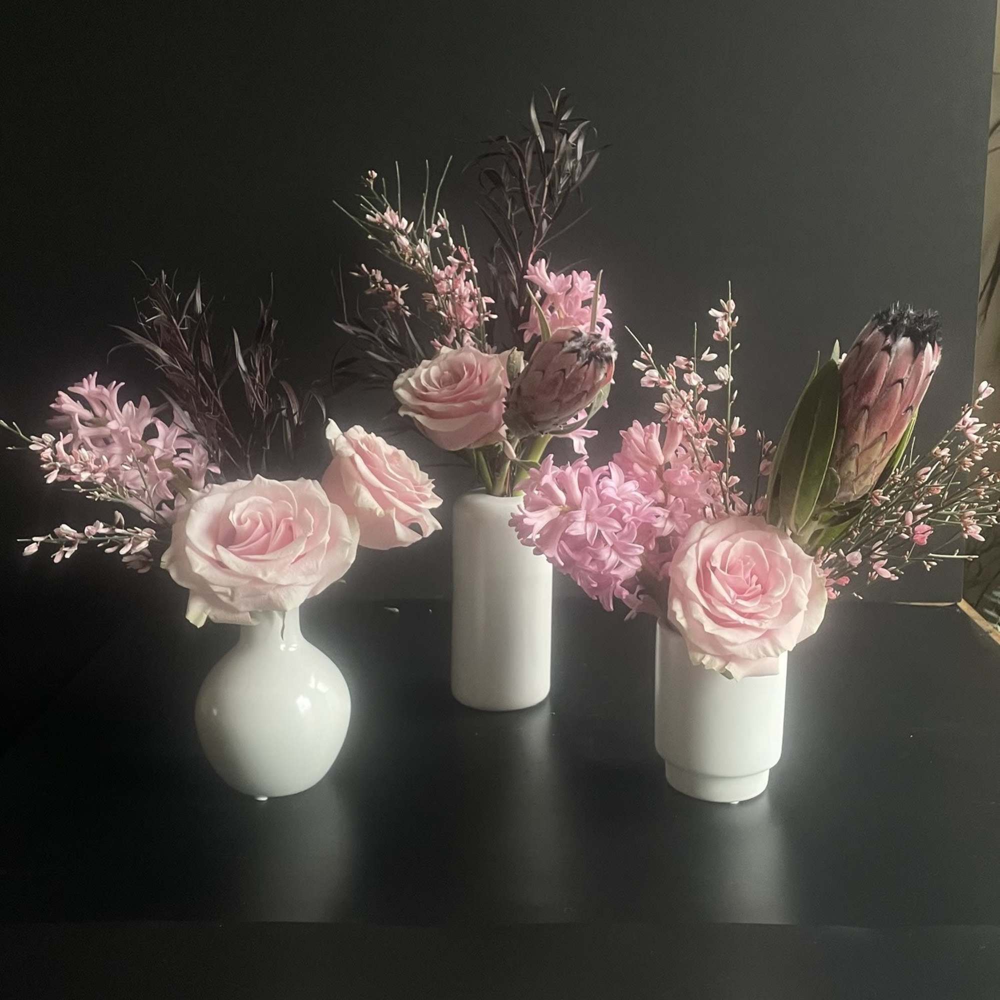 Three small pink floral arrangements in white vases on a dark surface