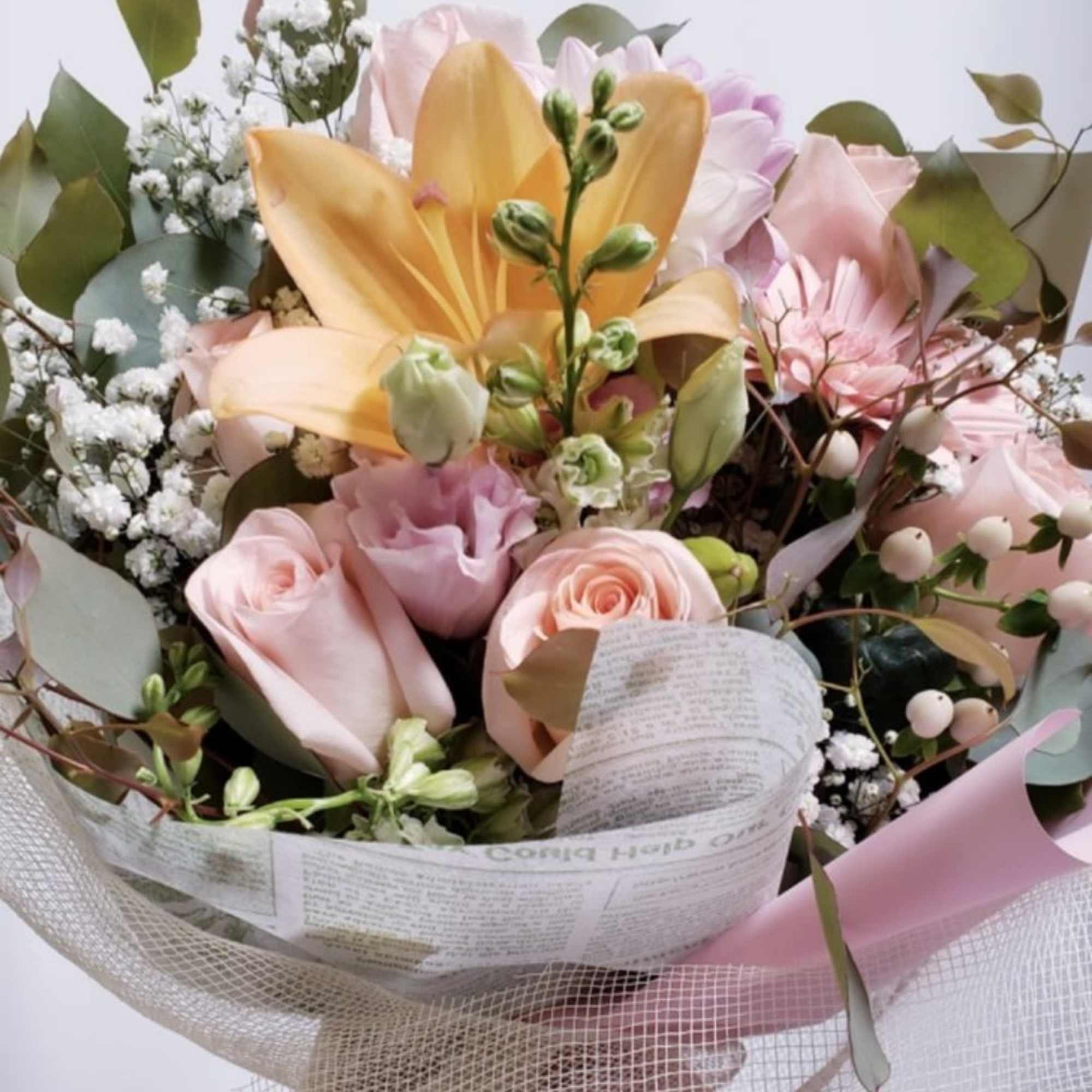 Bouquet of pink roses, lilies, and white filler flowers wrapped in paper