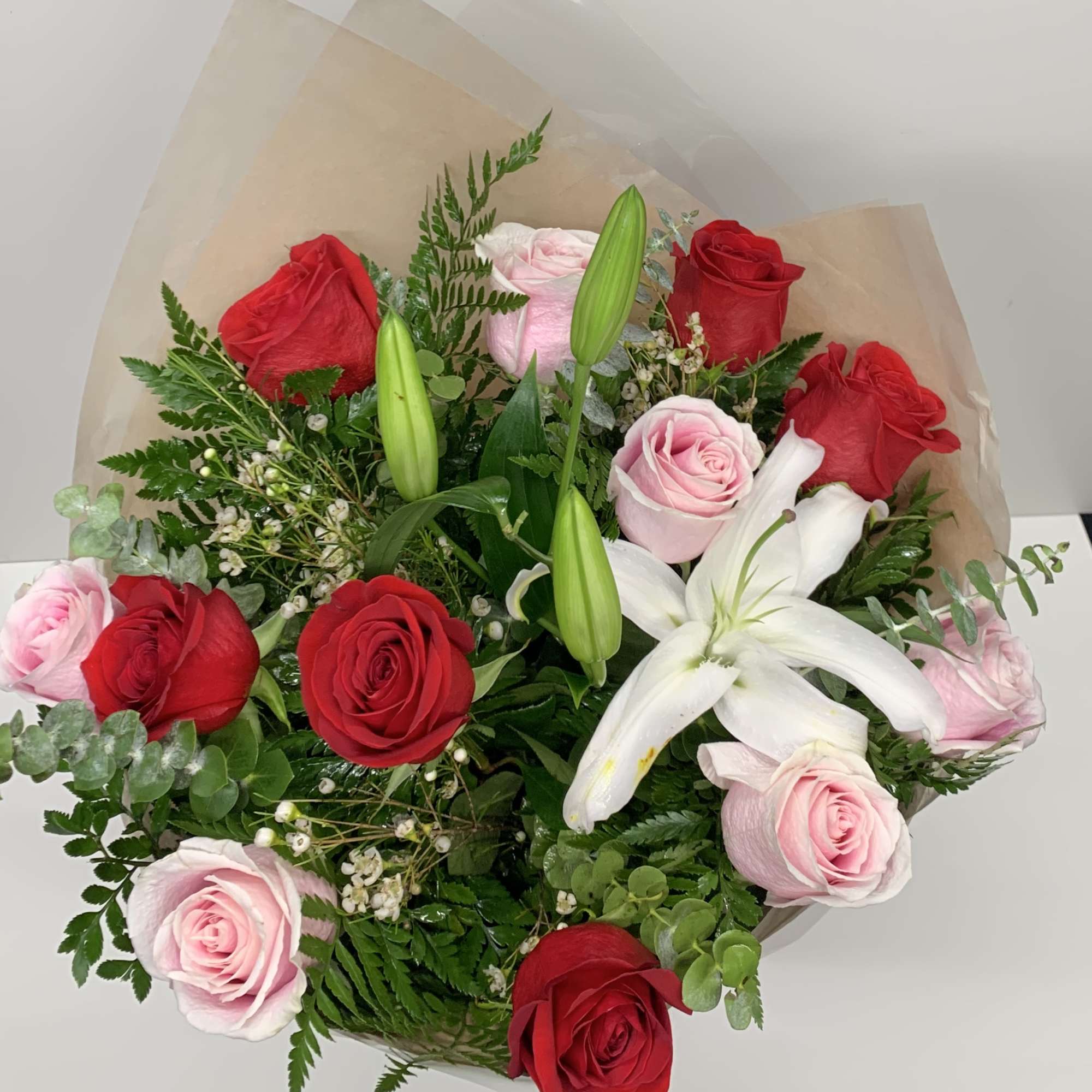 Bouquet of red and pink roses with white lilies in tan wrap