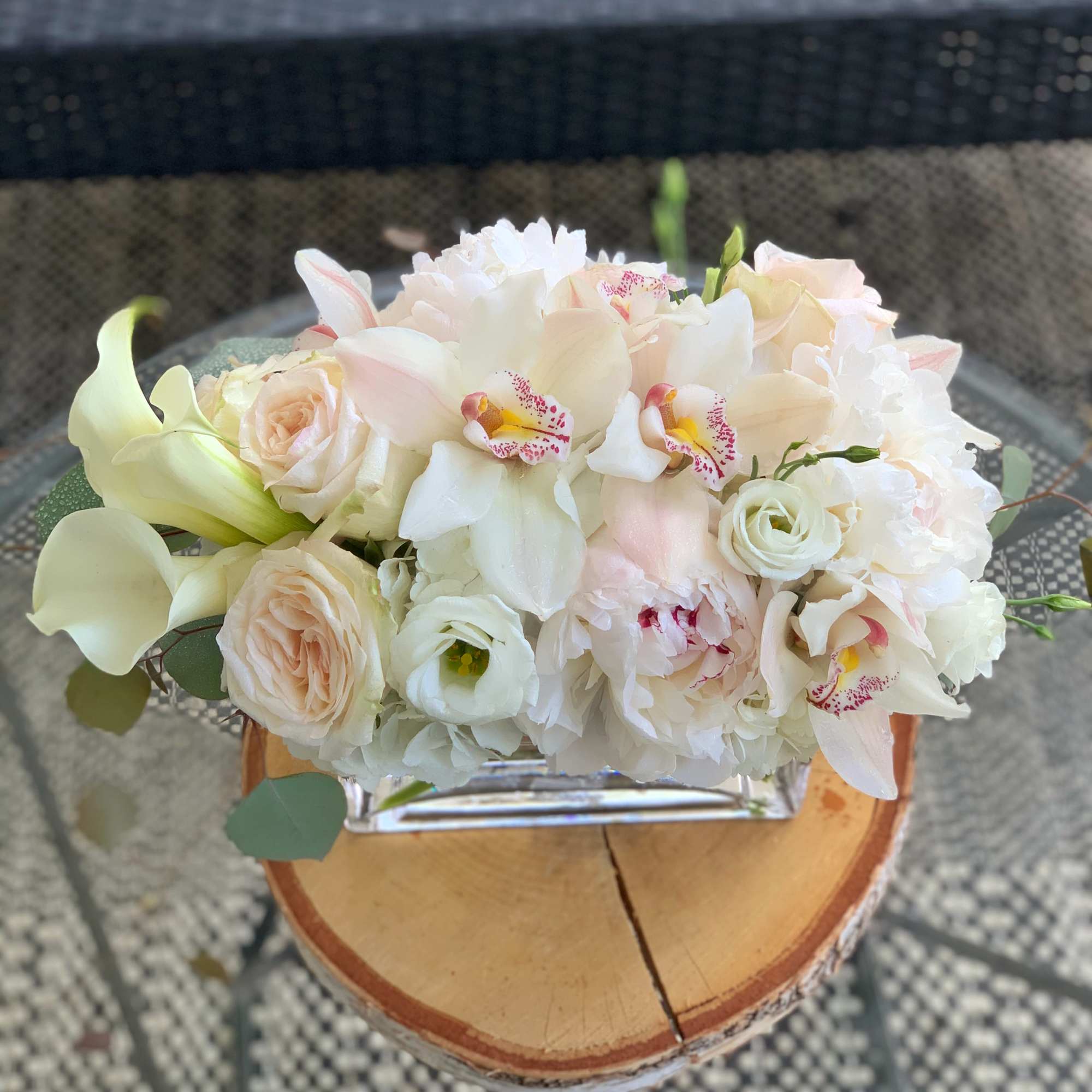 White and blush floral arrangement in a clear vase on a wood slice base