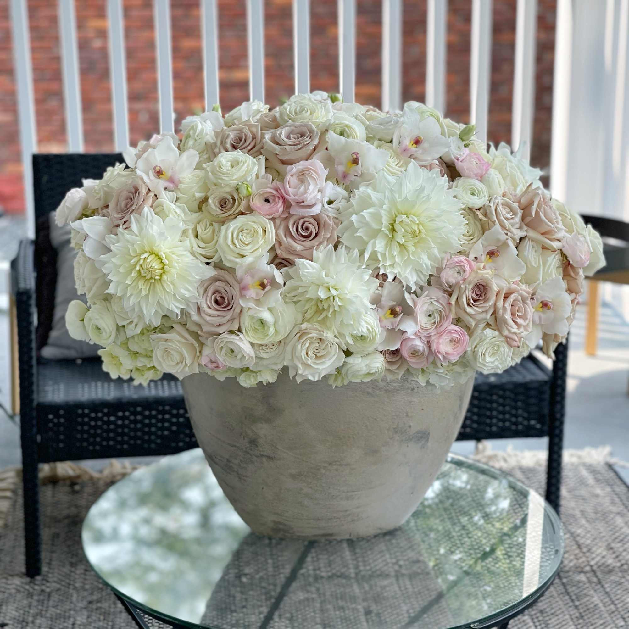Large pastel floral arrangement in a gray pot on a glass table