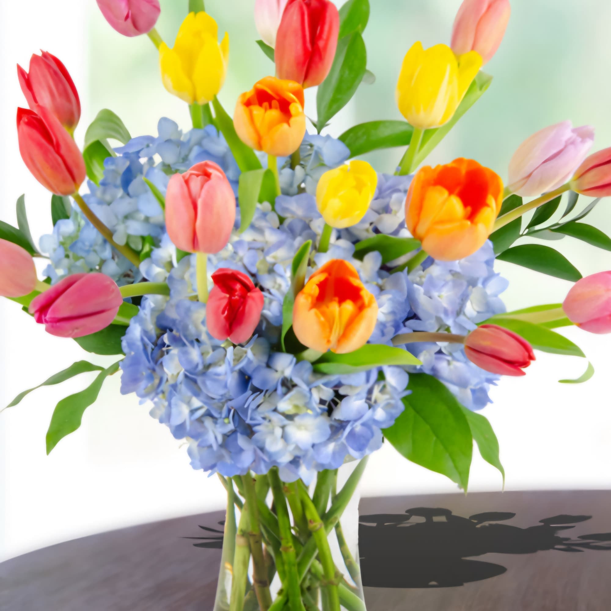 Colorful tulips arranged in a glass vase with blue hydrangeas