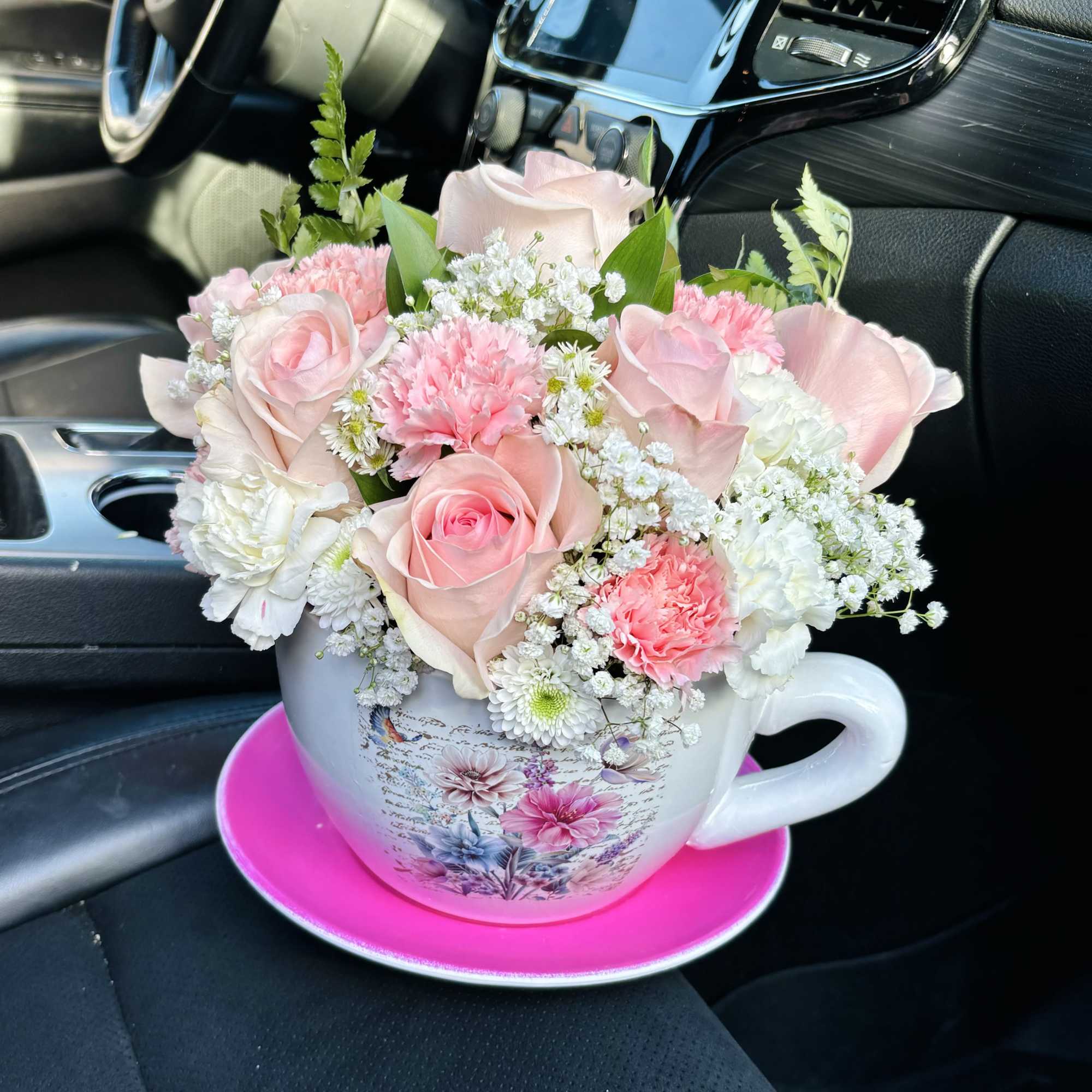 Pink and white flower arrangement in a teacup on a saucer