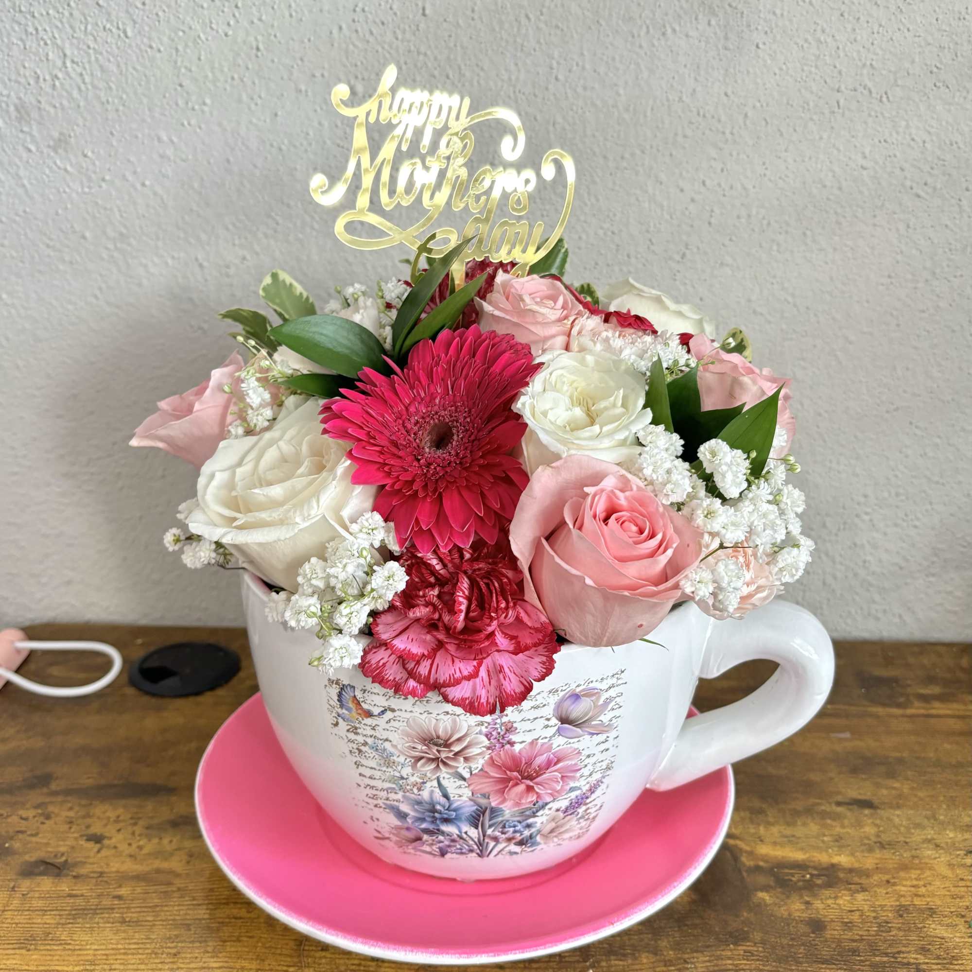 Pink and white flower arrangement in a teacup with a Mother's Day topper