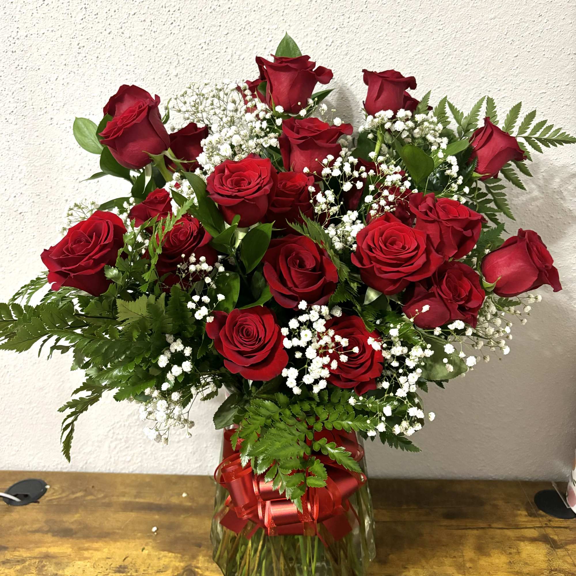 Red roses in a glass vase with baby's breath and a red ribbon