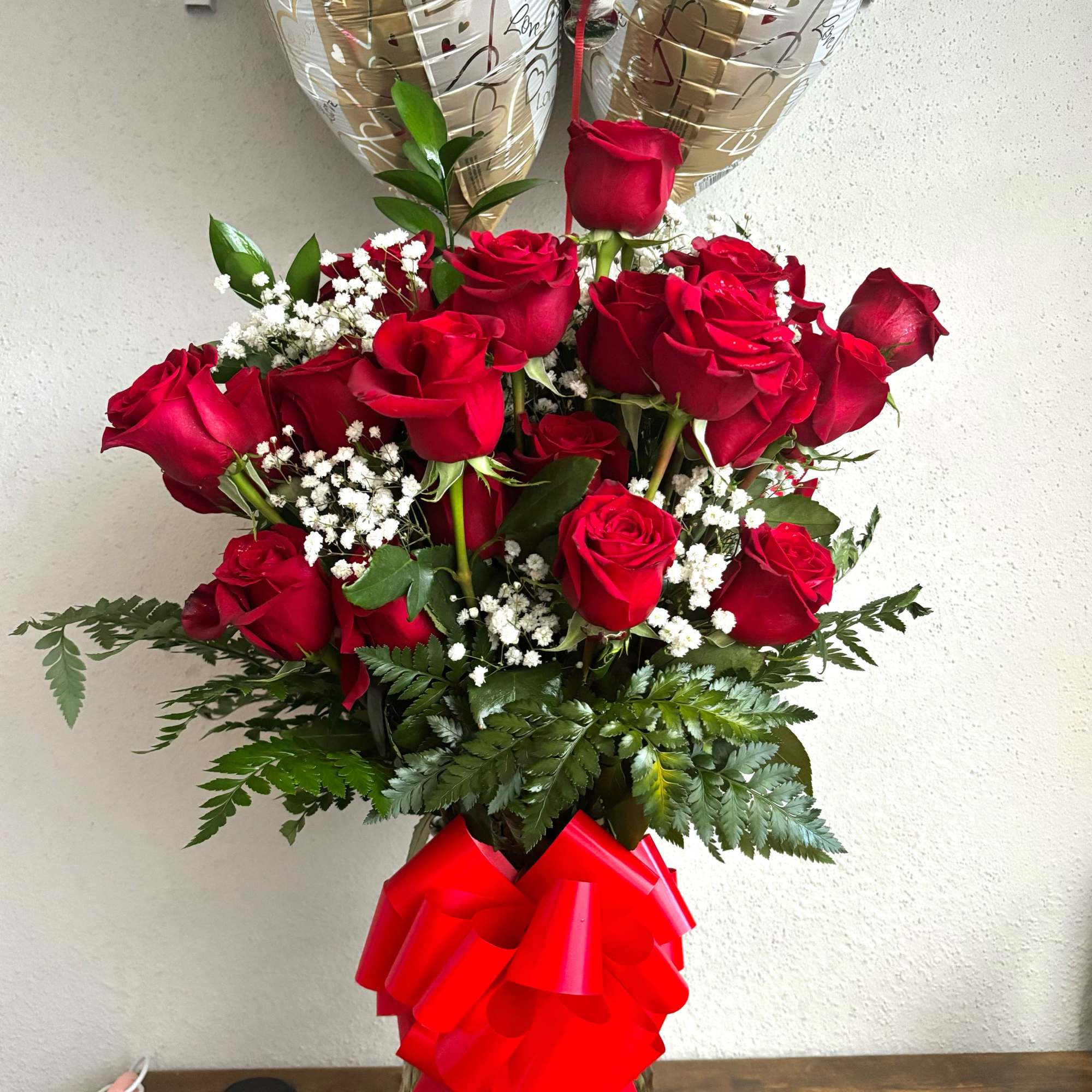 Bouquet of red roses with gold heart balloons in a glass vase