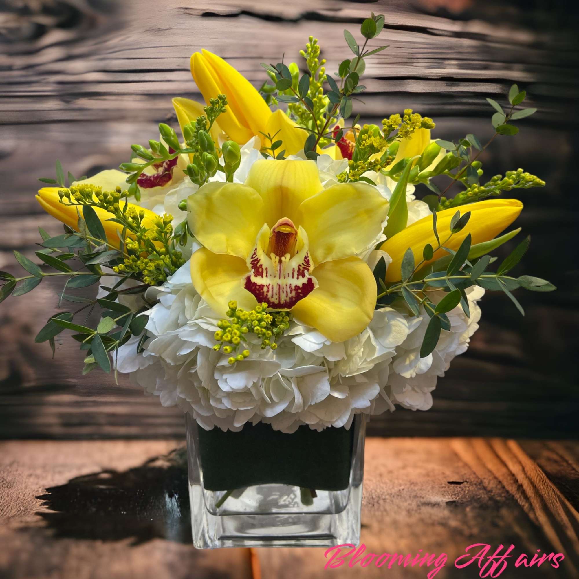Yellow orchids and white hydrangeas in a clear square vase