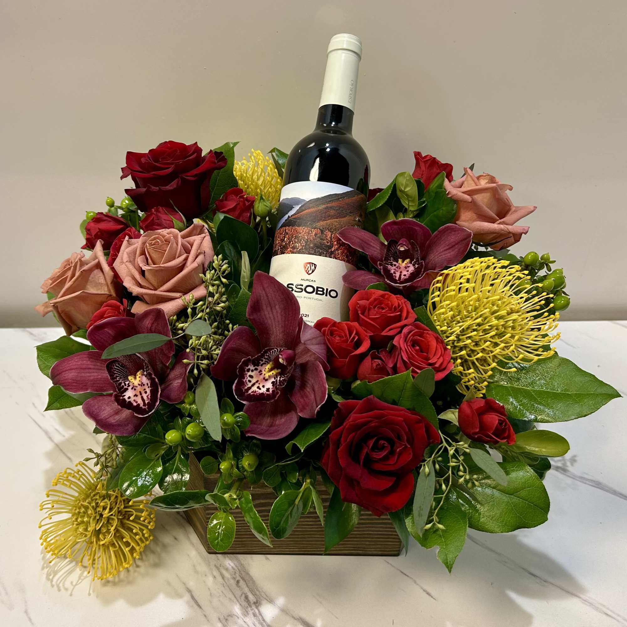 Wine bottle surrounded by red and blush roses with orchids and yellow blooms