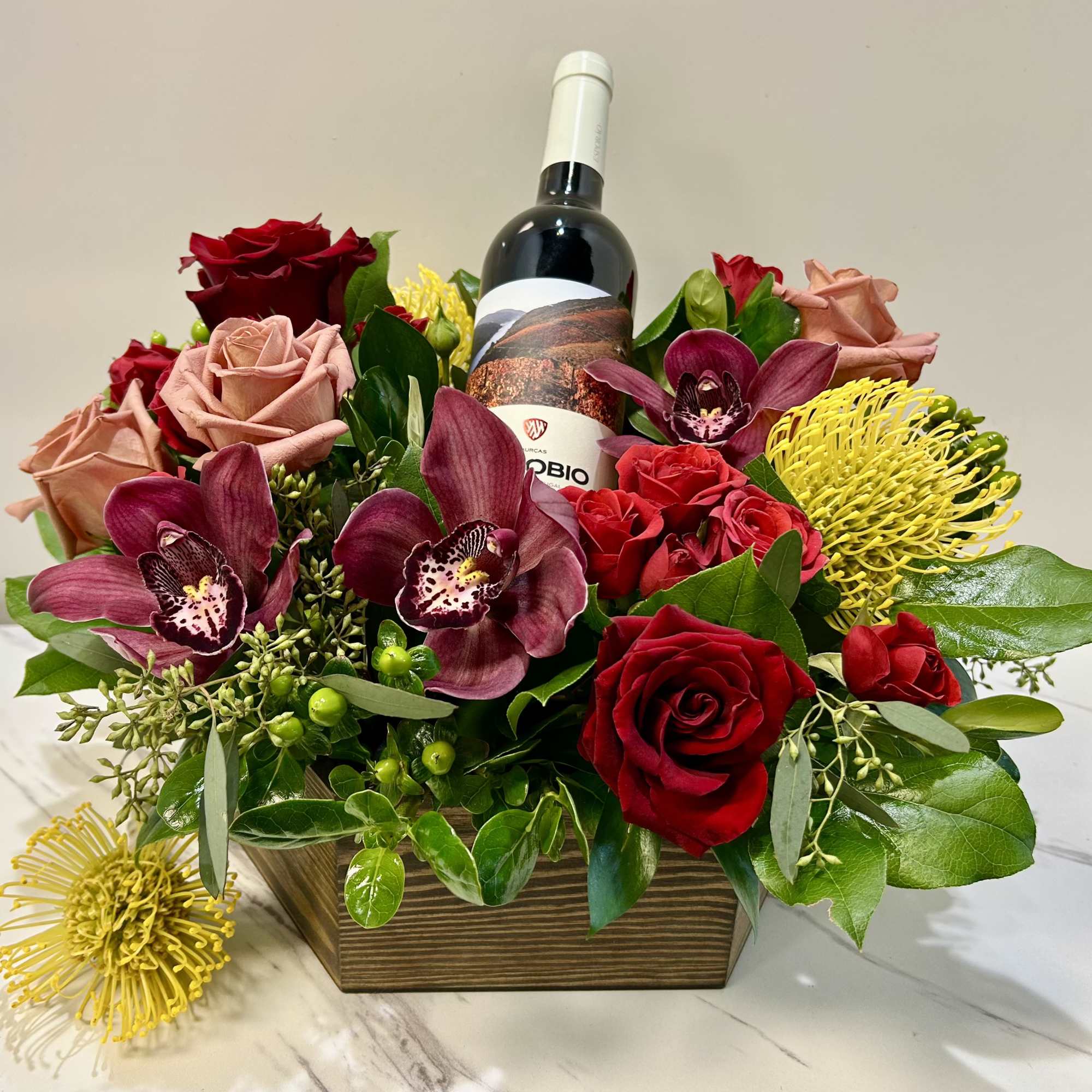 Floral arrangement with roses, orchids, and a wine bottle in a wooden box