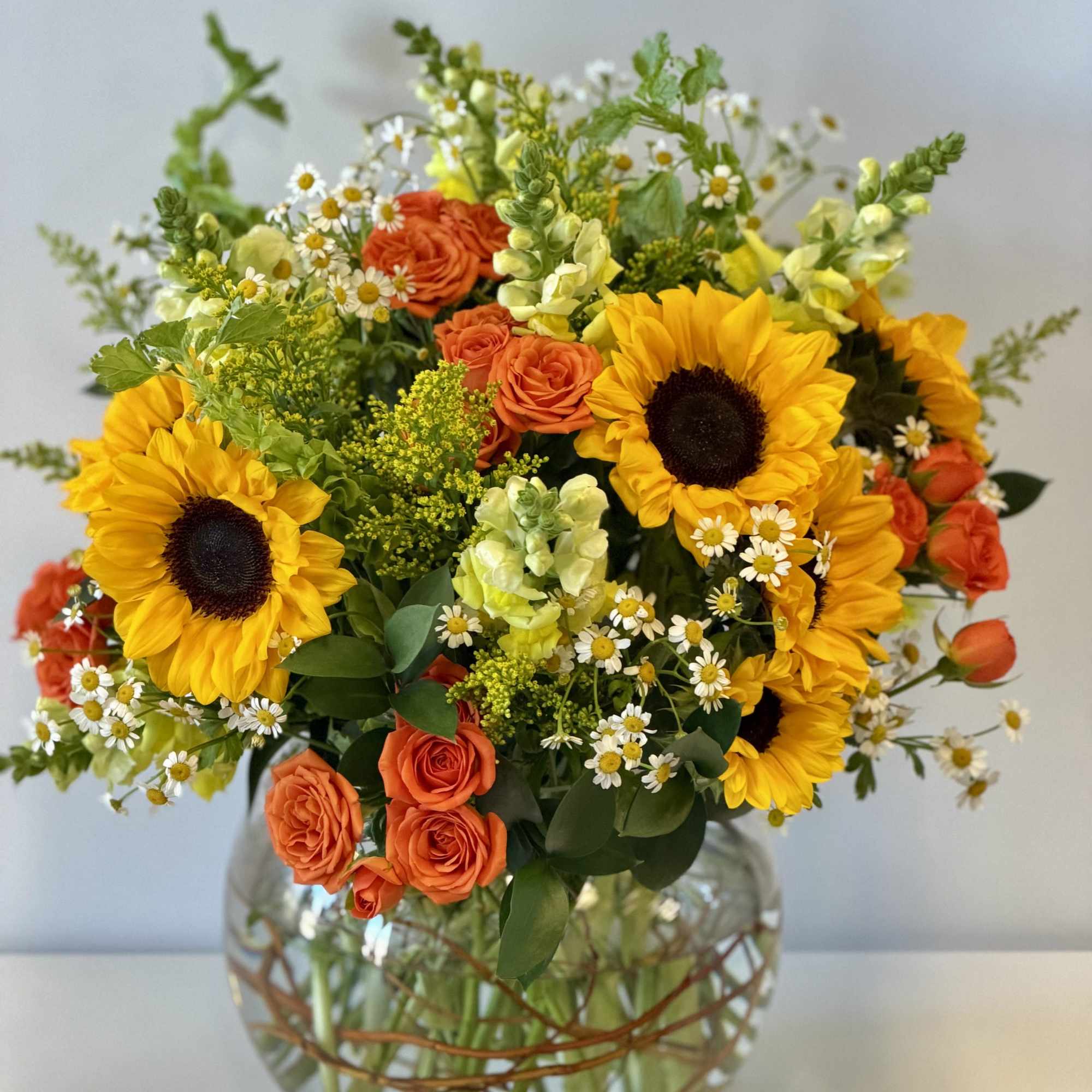 Bouquet of sunflowers, orange roses, and small white daisies in a glass vase