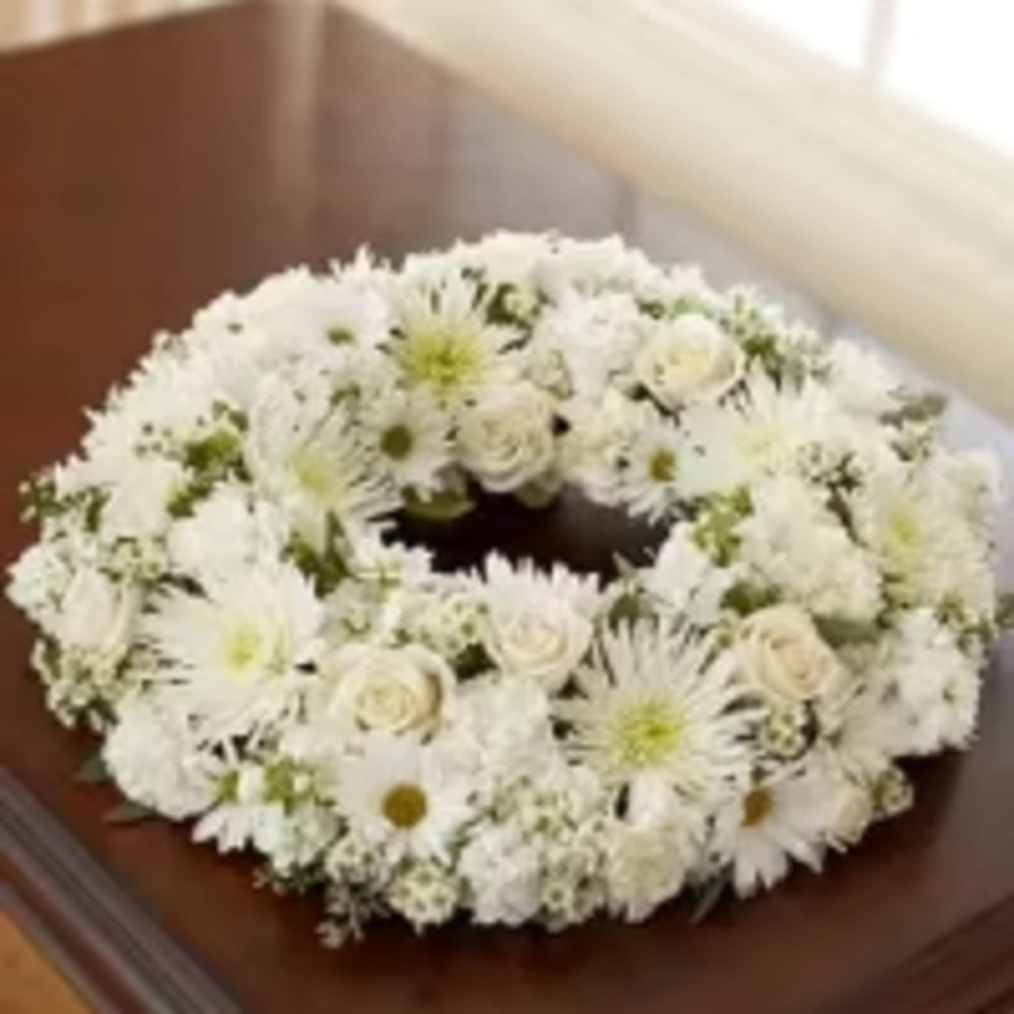 A low, circular sympathy wreath crafted in pure whites and soft greens