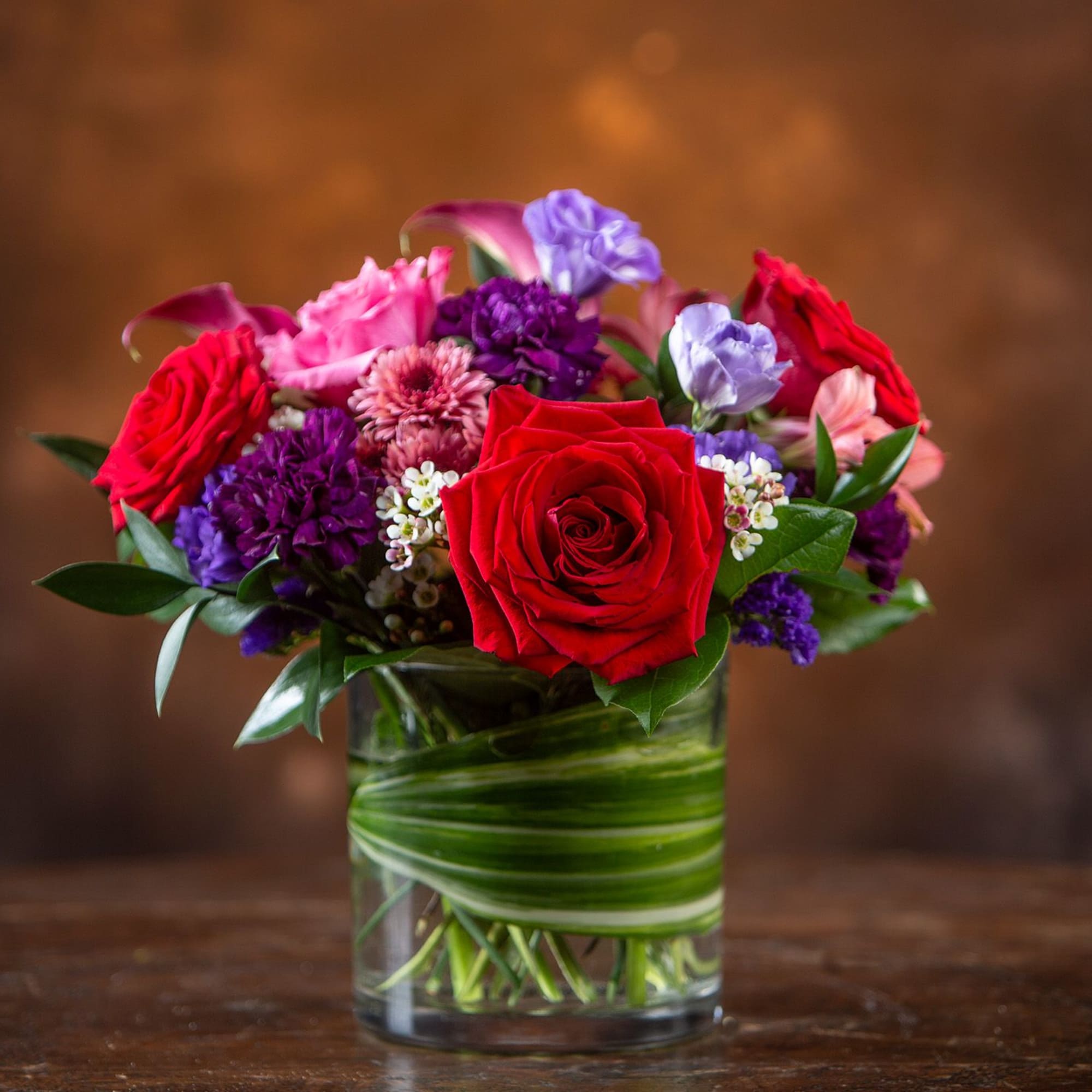 Mixed bouquet of red, pink, and purple flowers in a glass vase