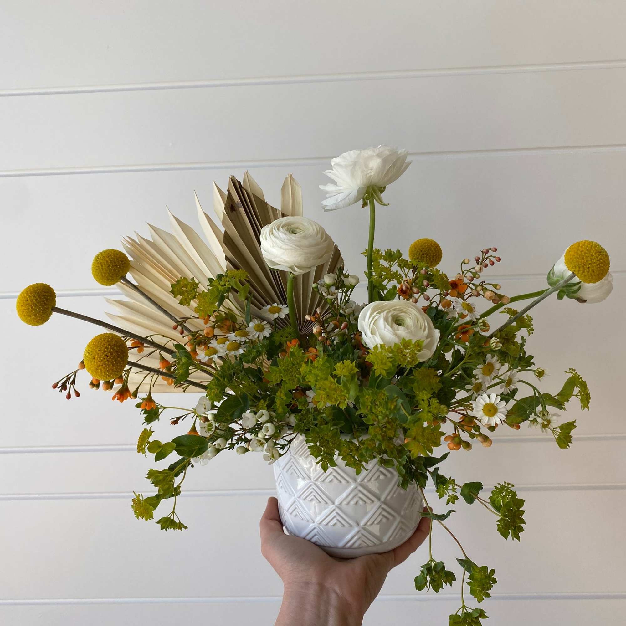 White floral arrangement in a textured white pot with yellow pom-pom blooms