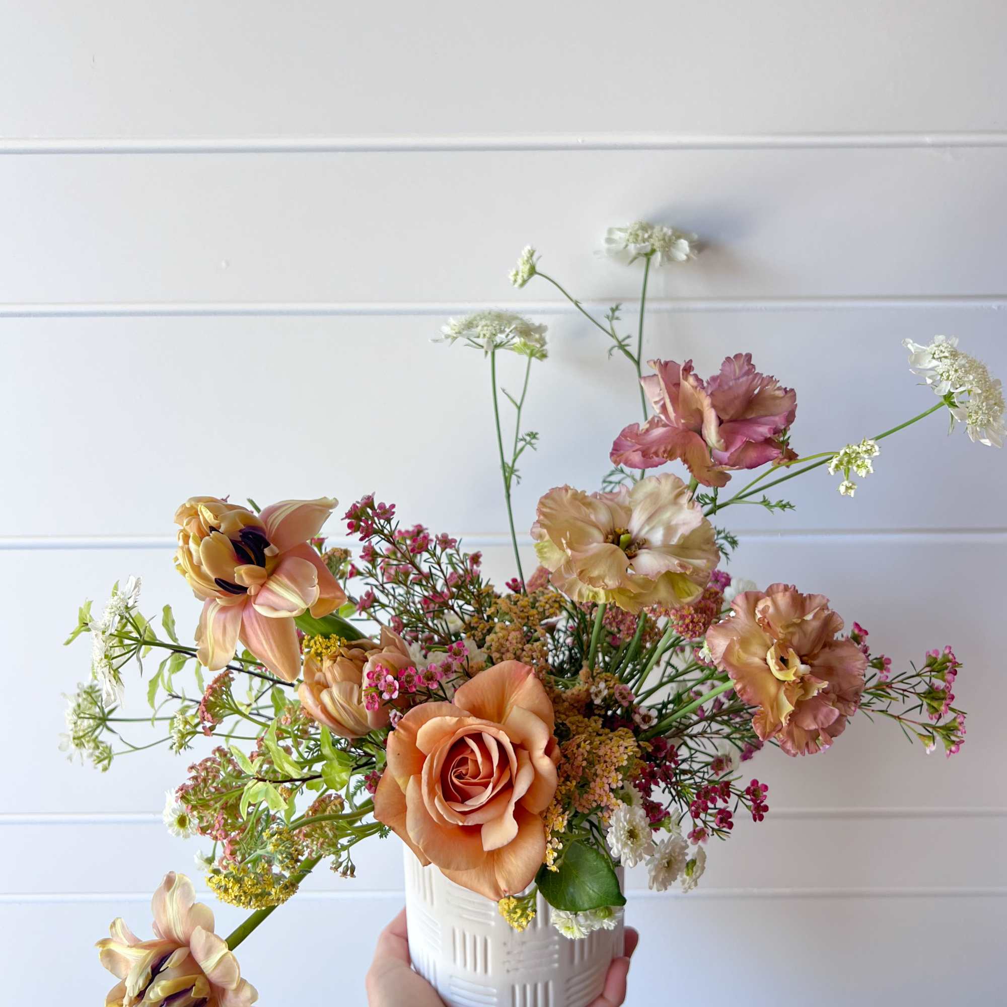 Peach and pink floral arrangement in a white ceramic pot