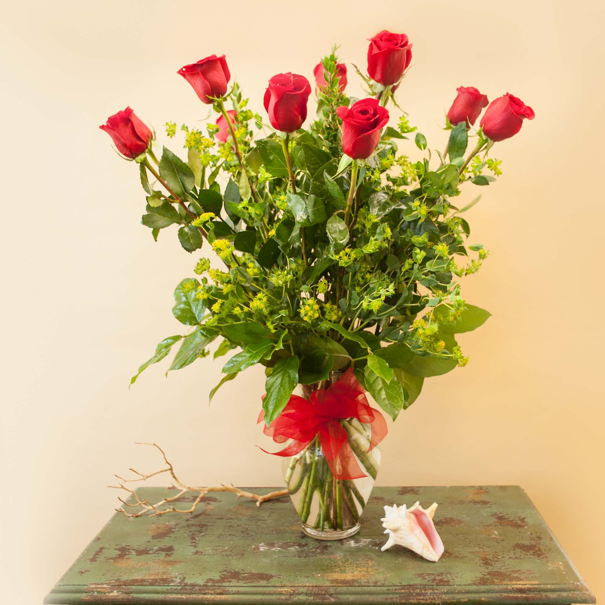 Tall bouquet of red roses in a clear glass vase with a red ribbon