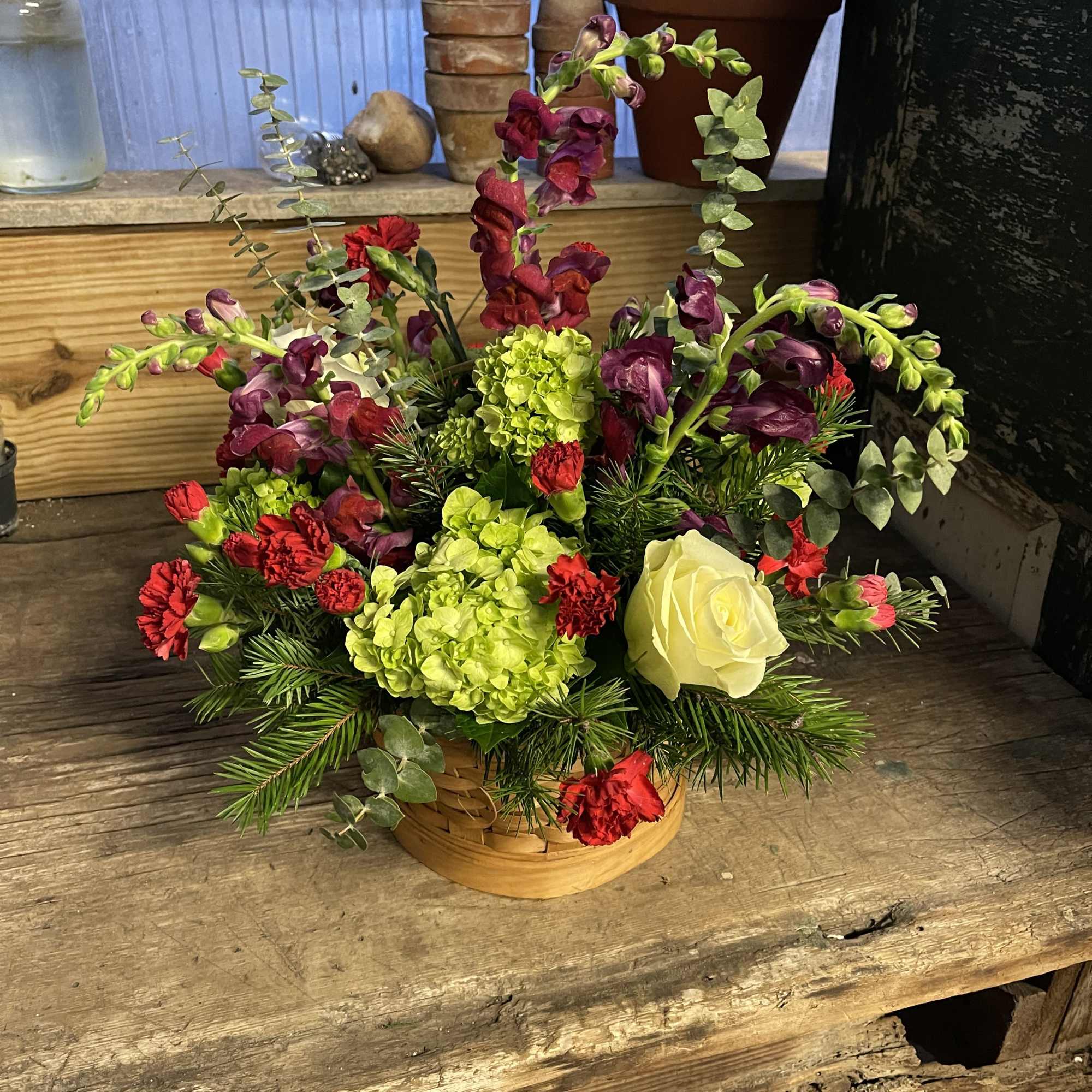 Mixed floral arrangement in a low basket with red, green, and purple blooms