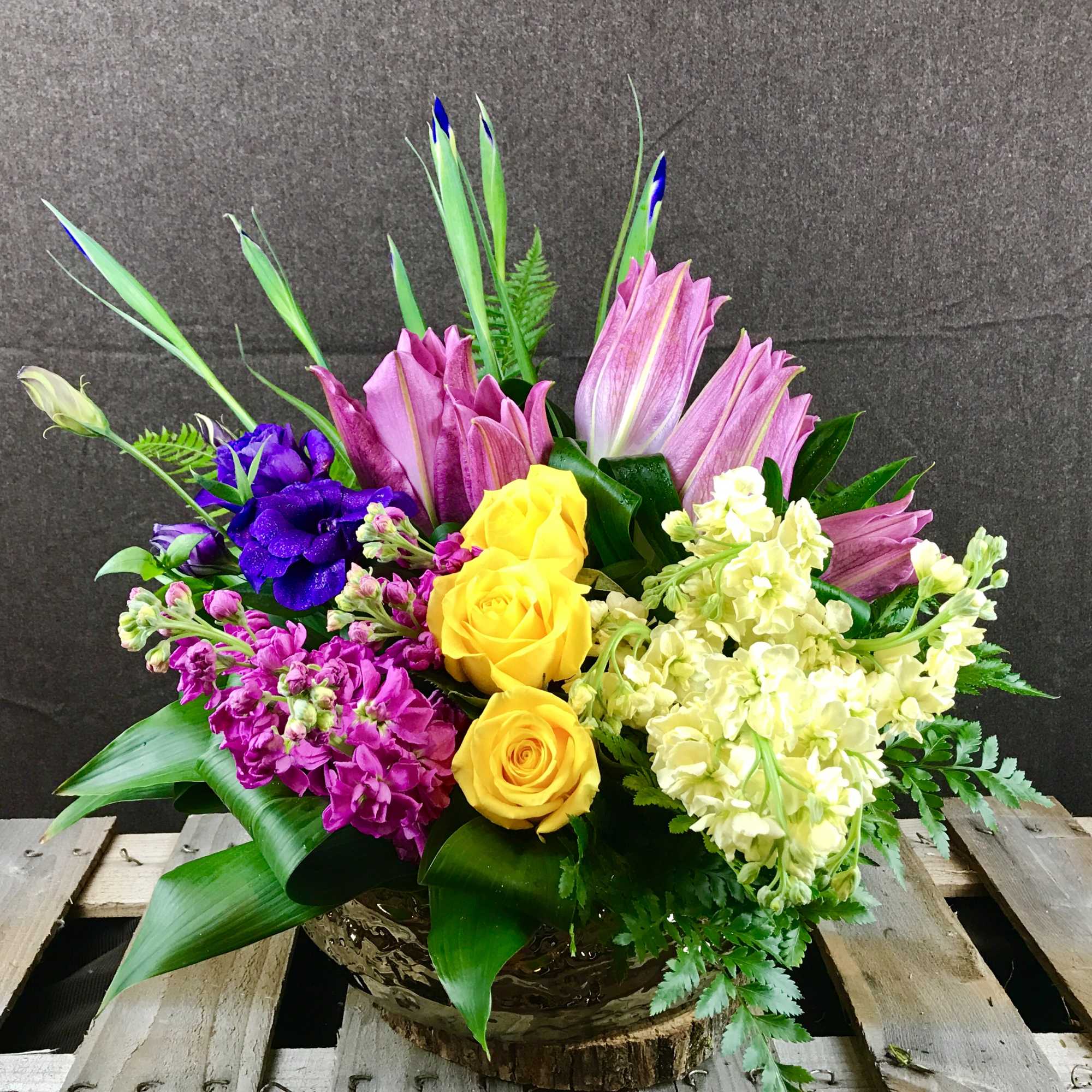 Colorful bouquet with yellow roses, pink lilies, and purple flowers in a low container