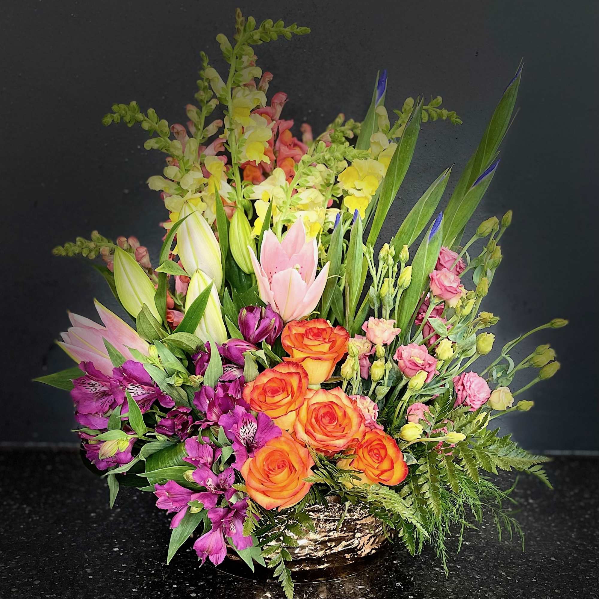 Mixed bouquet of orange roses, pink lilies, and purple flowers in a low container
