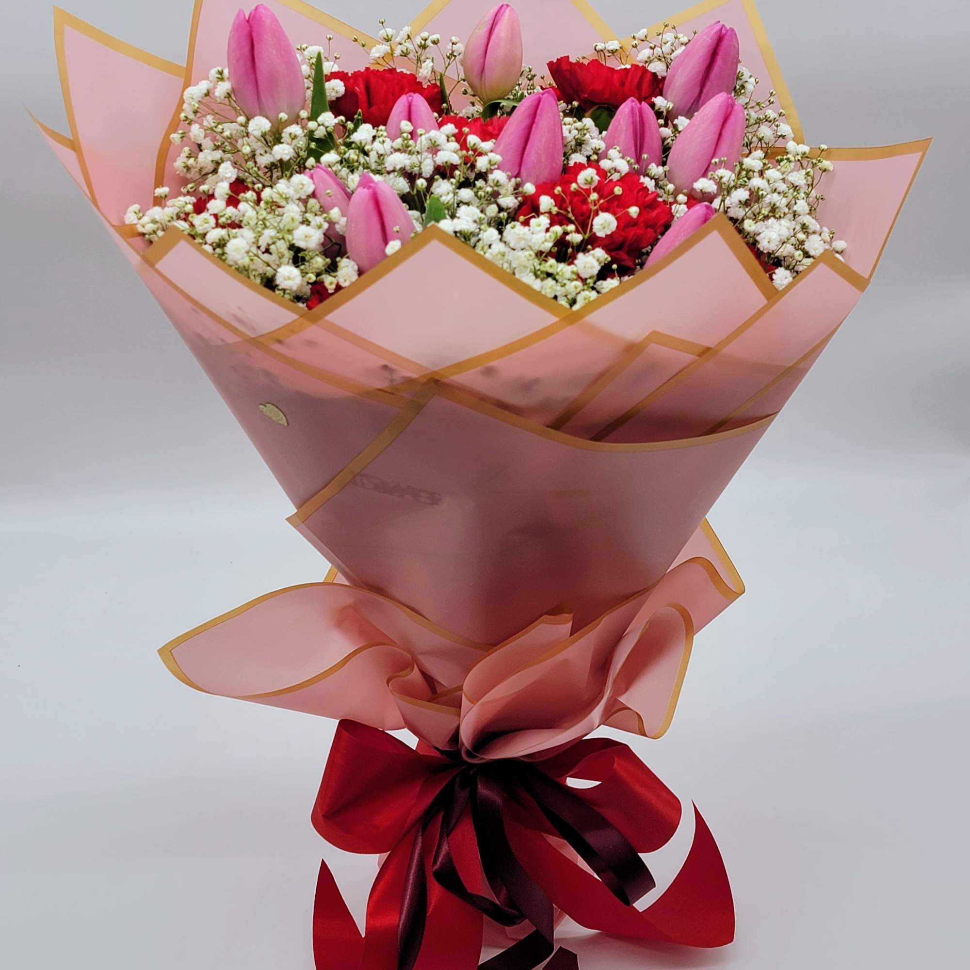 Pink tulips and red carnations in pink wrapping with a red ribbon
