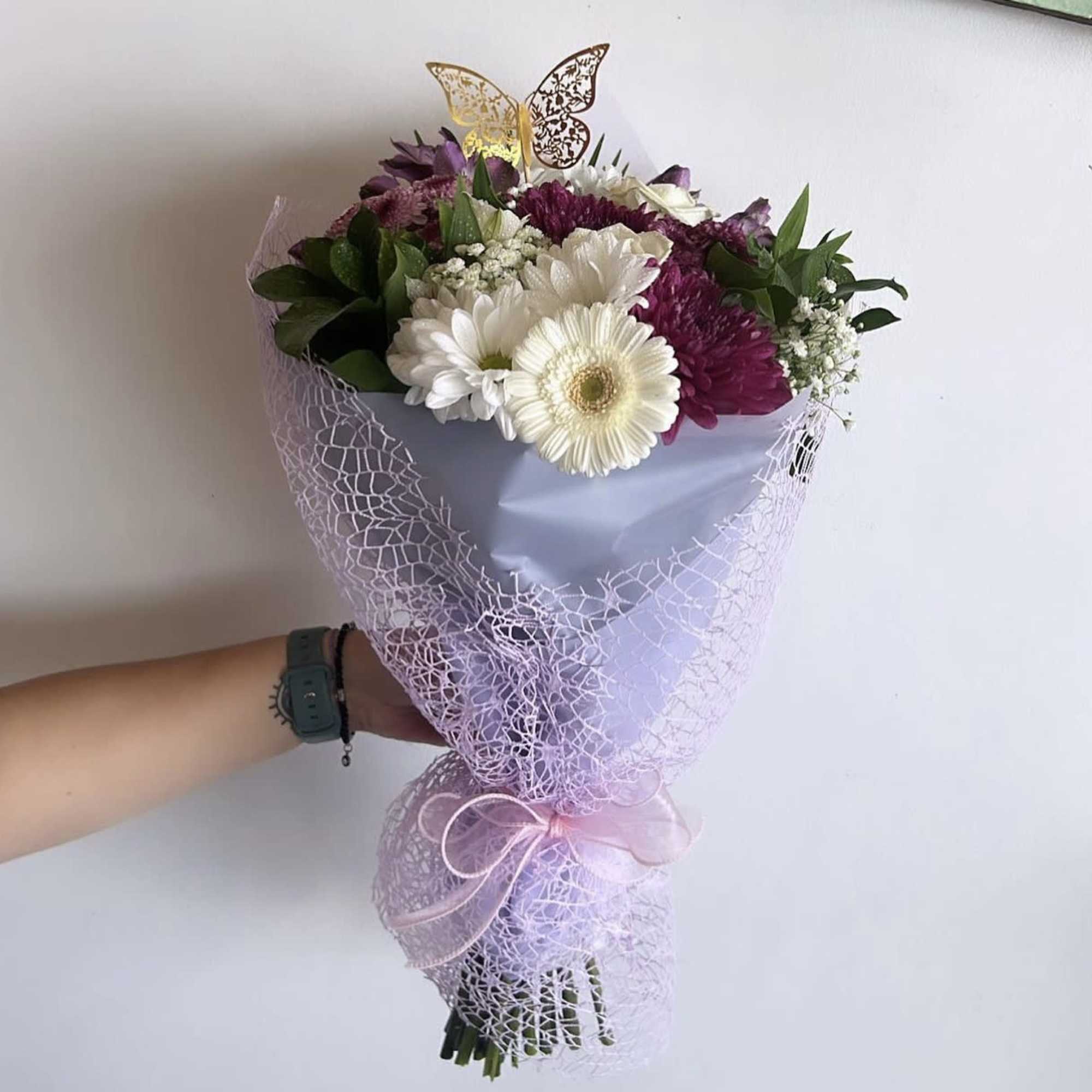 Handheld bouquet of white and purple daisies wrapped in lilac mesh
