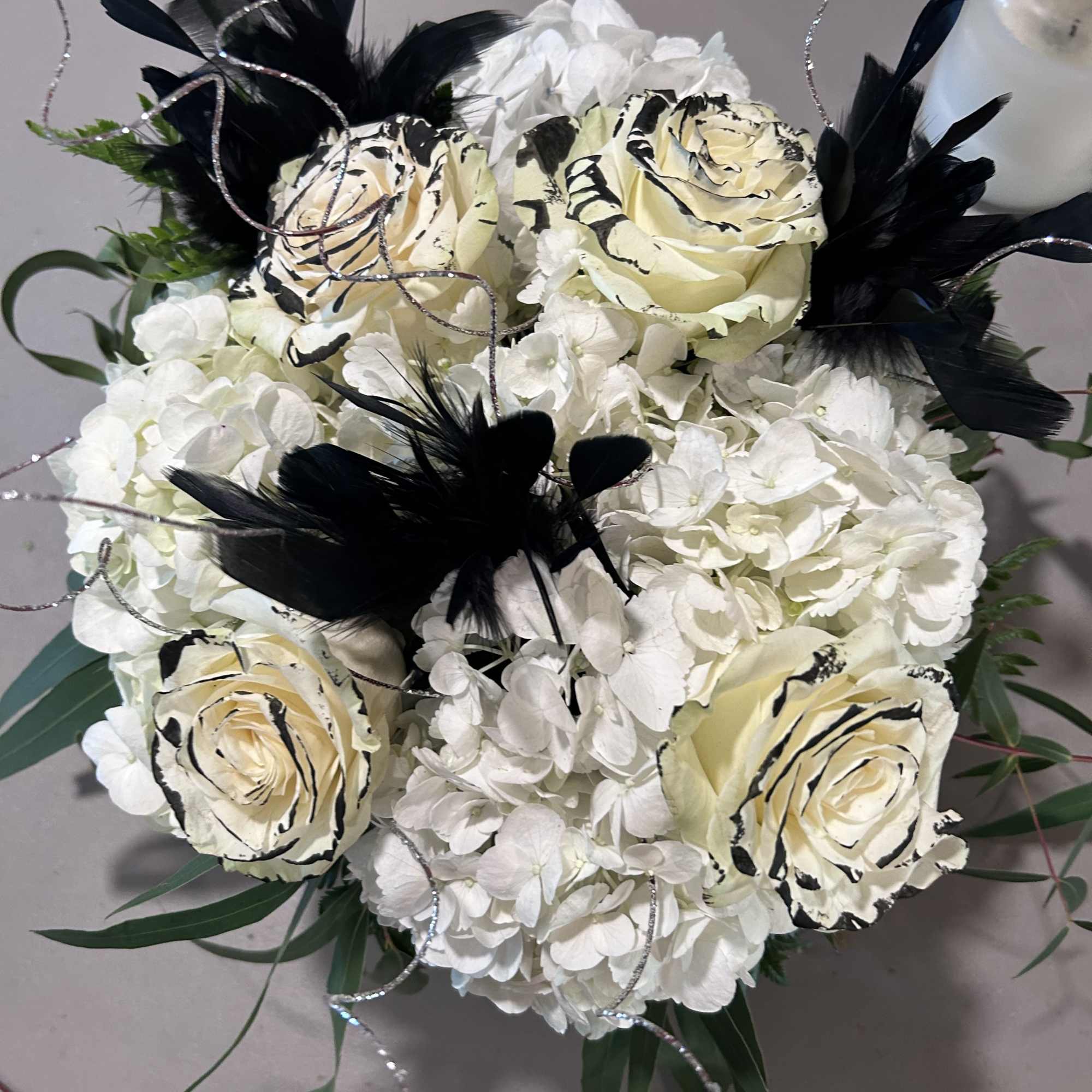 White floral bouquet with cream roses and black feather accents