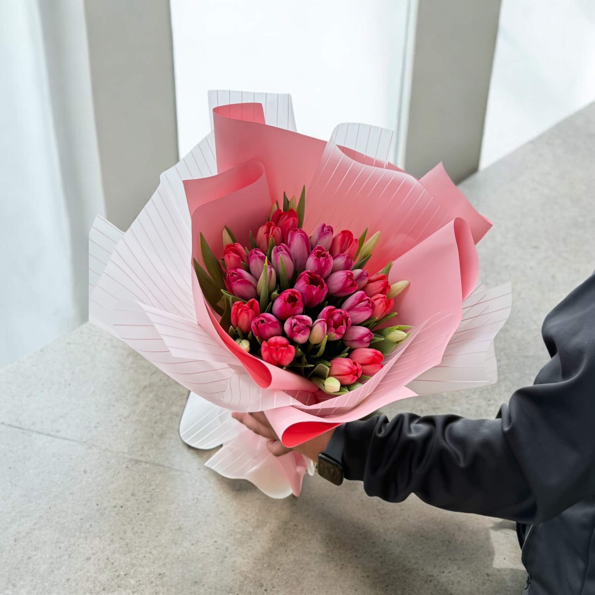 Handheld bouquet of pink and magenta tulips wrapped in pink paper