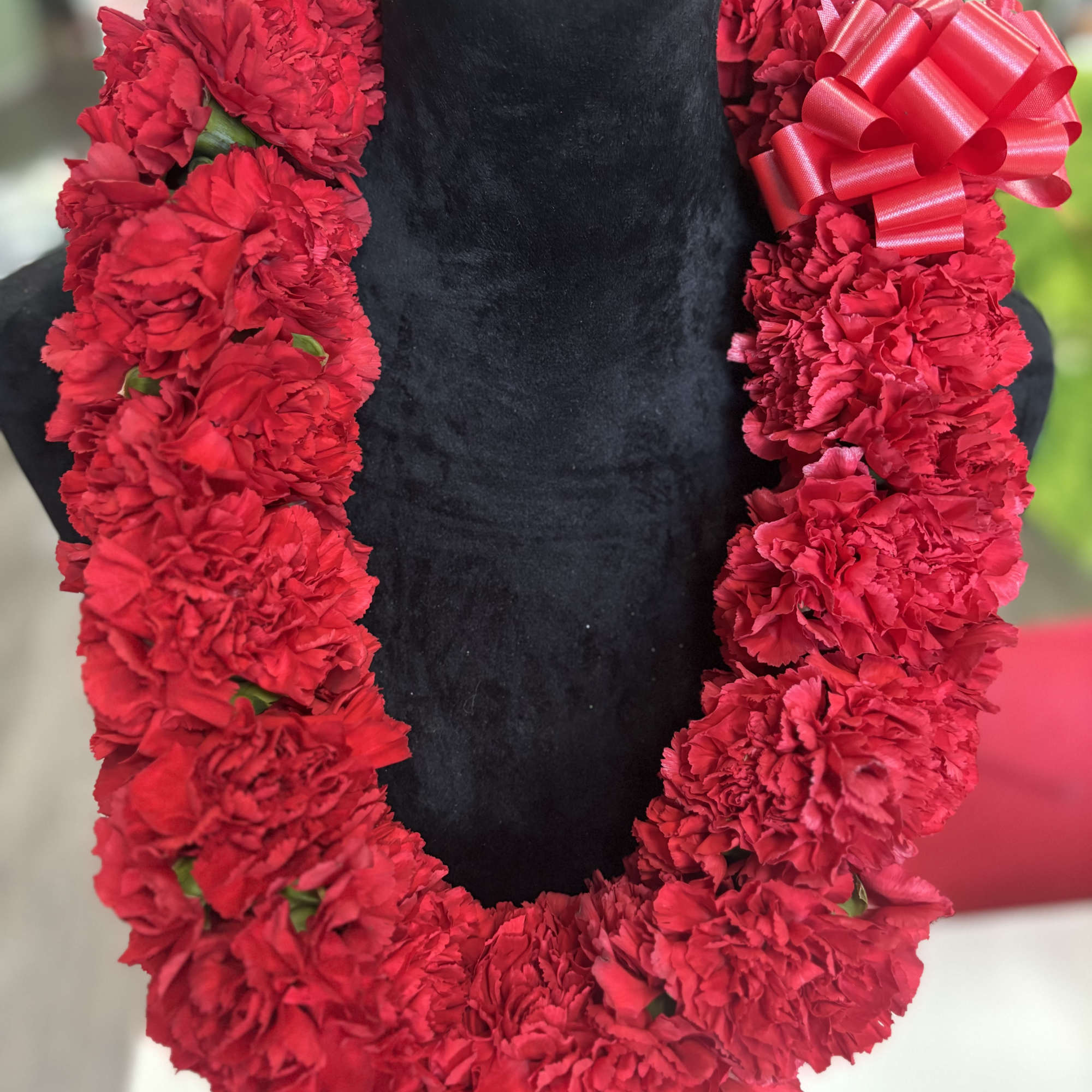 Red carnation lei with a satin bow on a black display bust