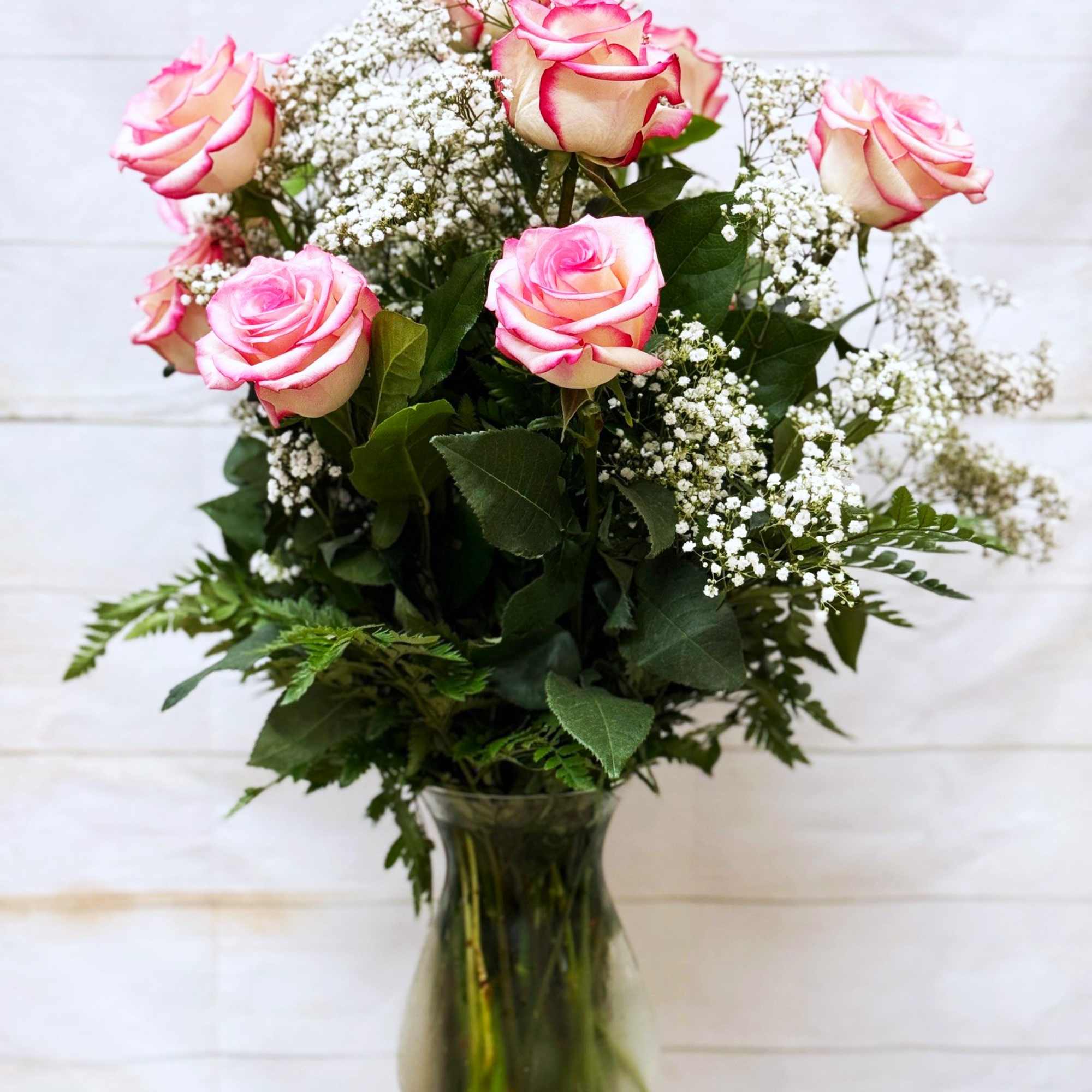 Tall arrangement of pink-tipped cream roses with white filler flowers in a clear glass vase