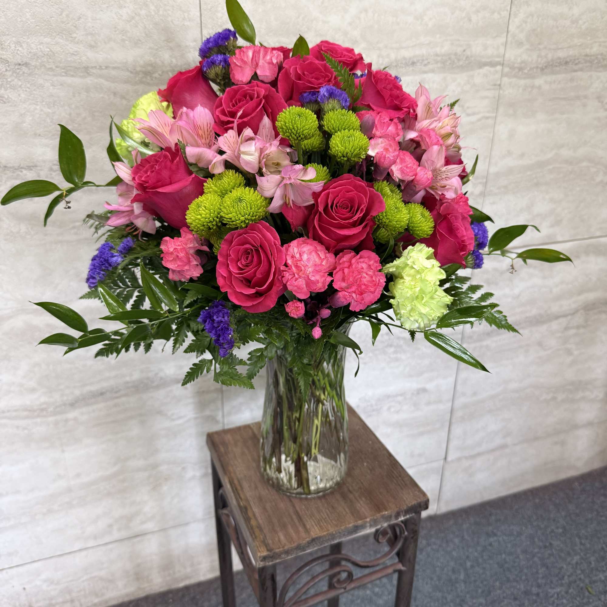 Bright pink roses, carnations, and mixed blooms in a clear glass vase on a small table