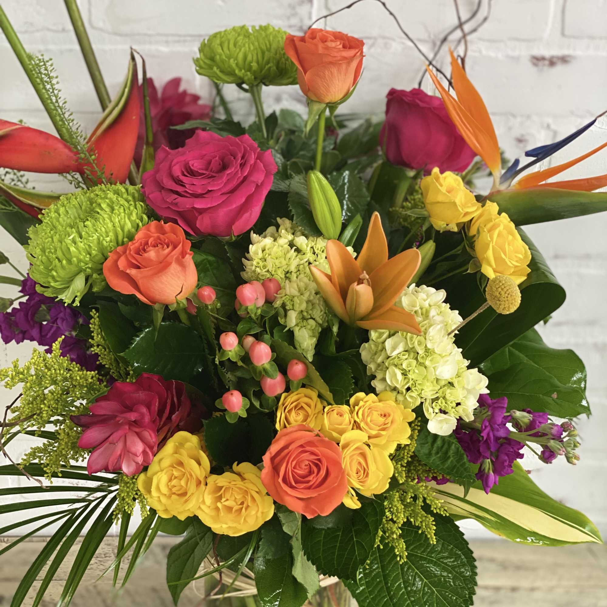 Colorful mixed bouquet with roses, orchids, and hydrangeas in a glass vase
