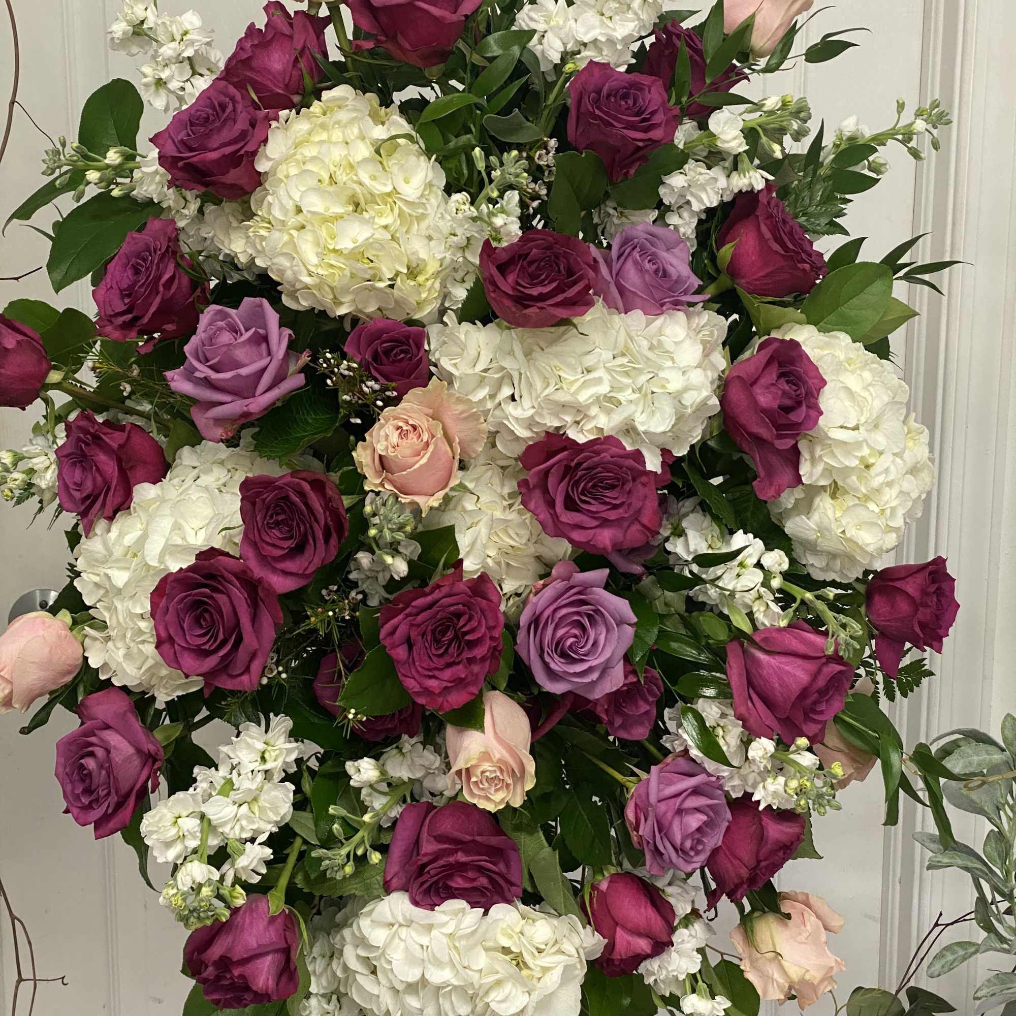Large standing spray of pink, purple, and white roses with white hydrangeas