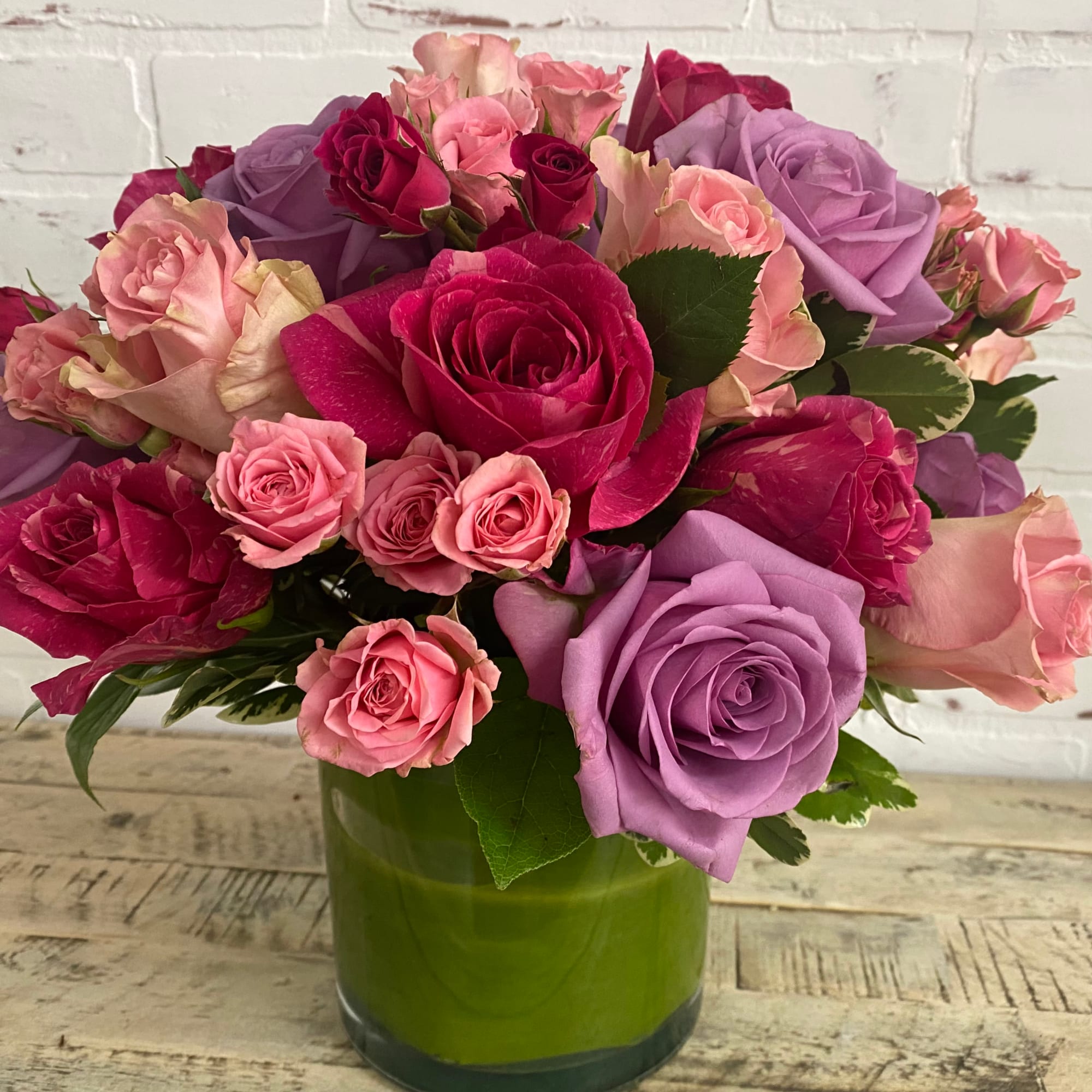 Bouquet of pink, purple, and red roses in a green glass vase