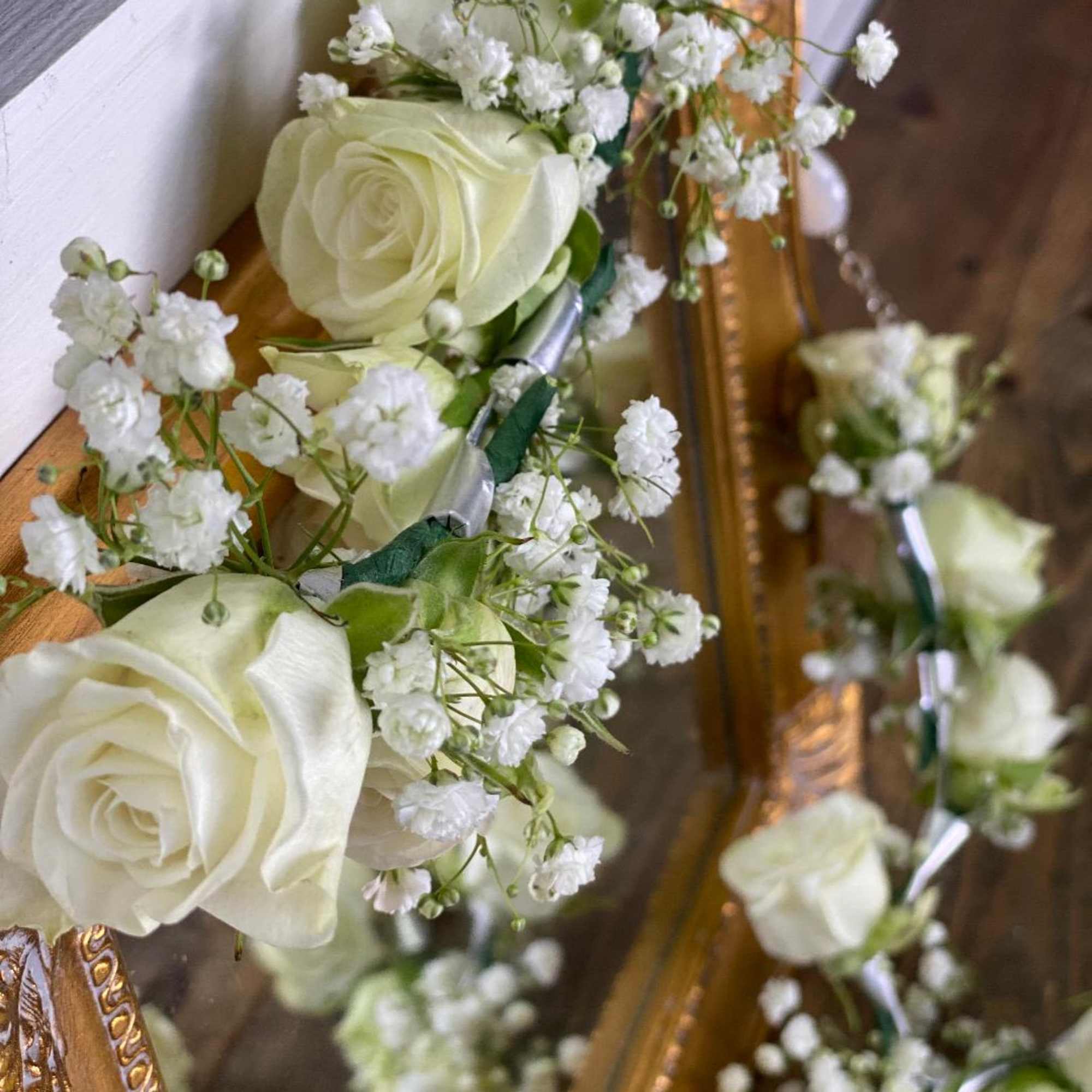 White rose floral garland with baby's breath draped over a gold-framed mirror