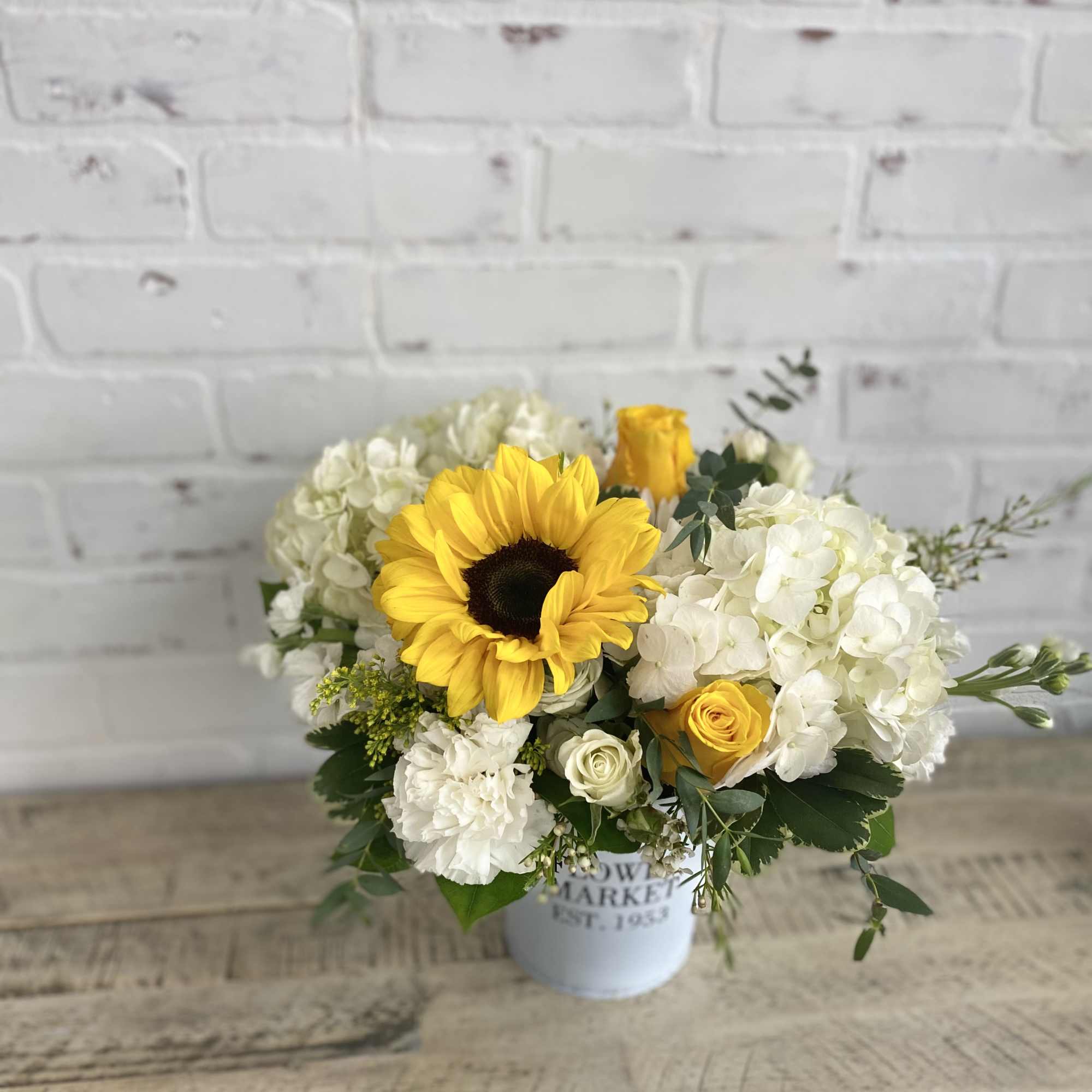 Bouquet of yellow sunflowers and white flowers in a white container