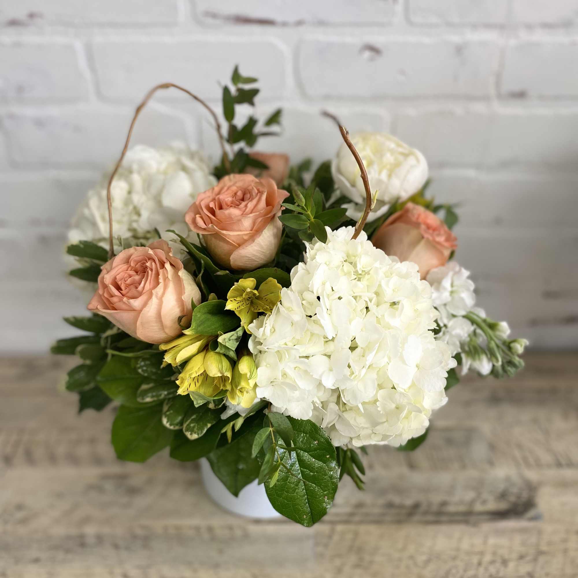 Peach roses and white hydrangea in a white container