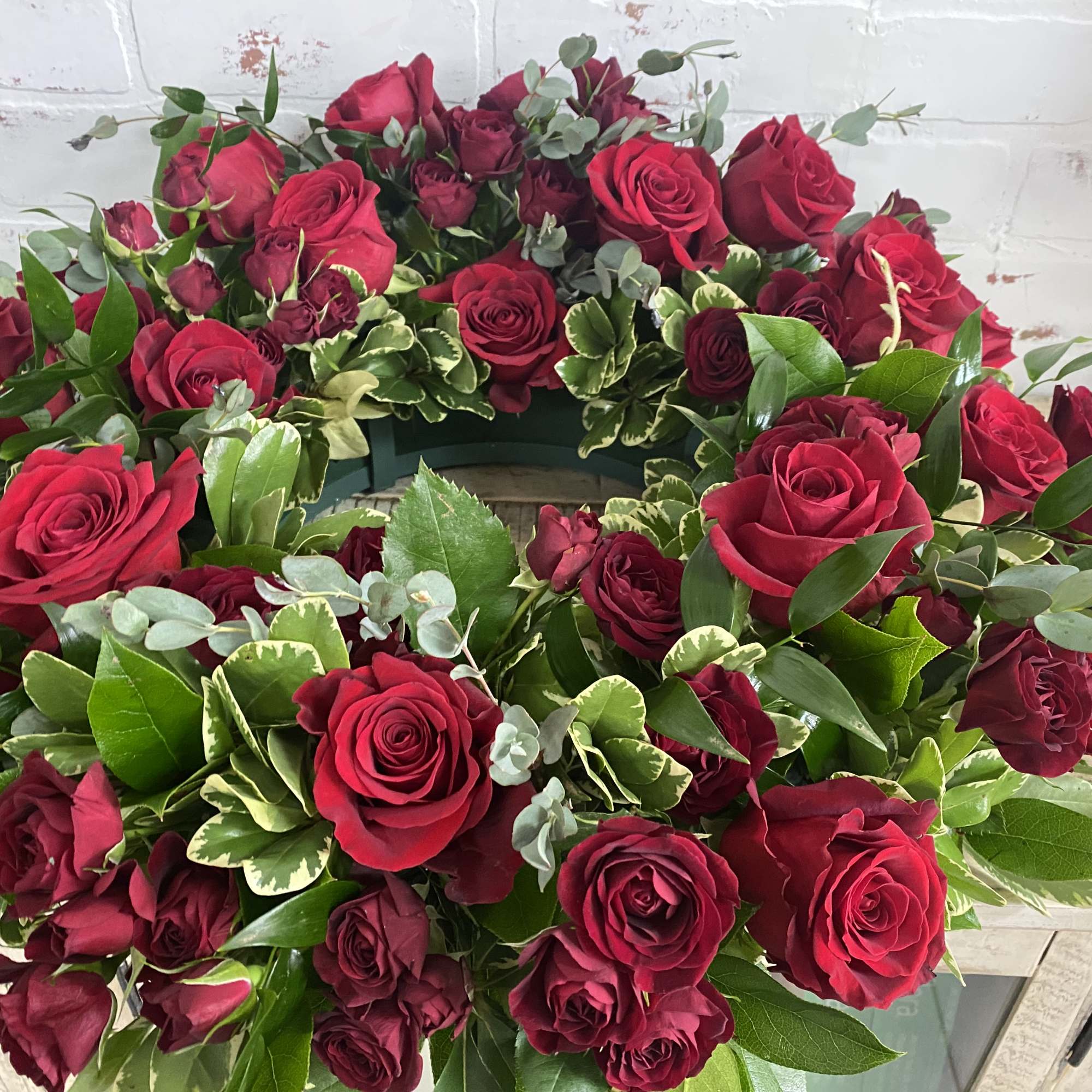 Circular wreath of red roses with mixed greenery on a white surface