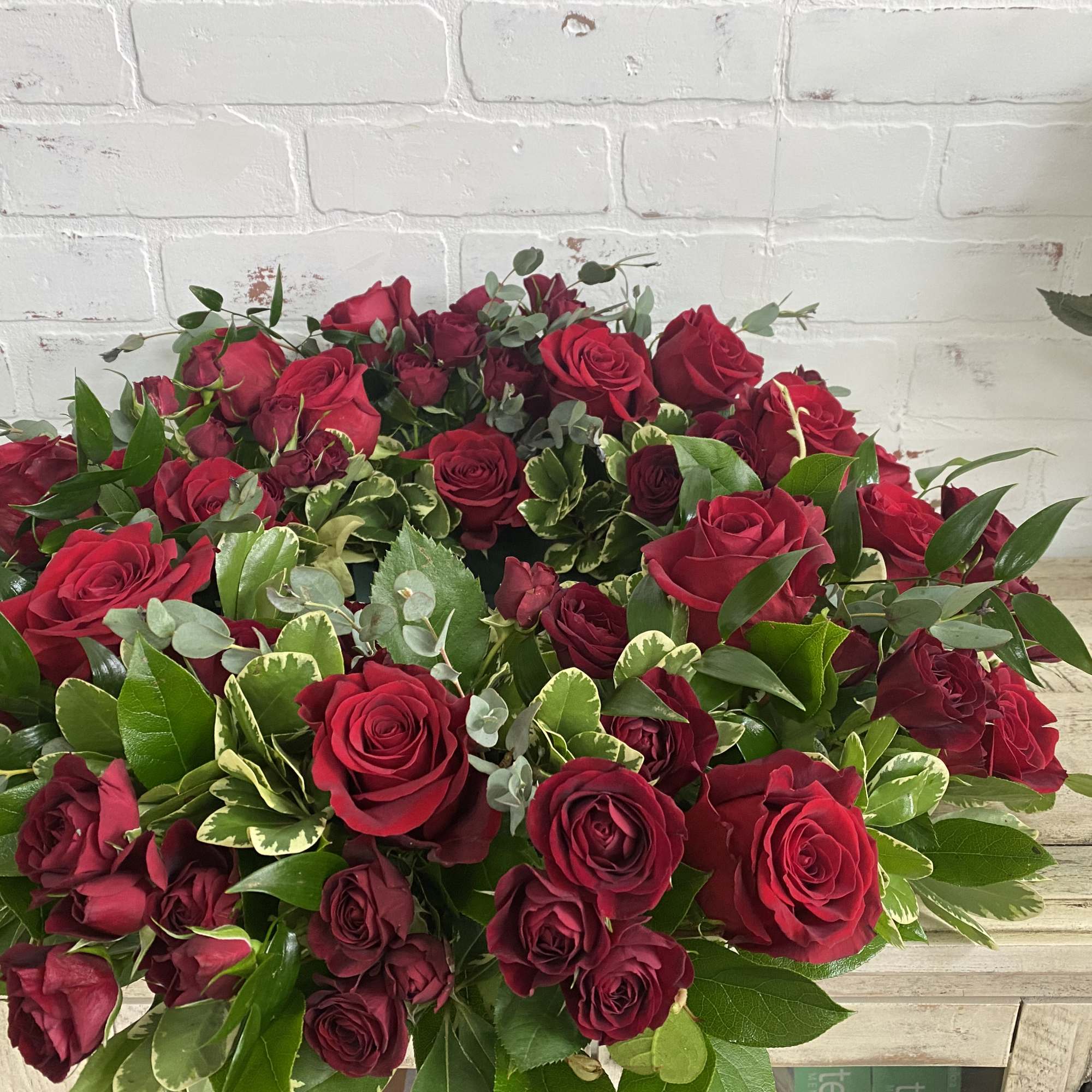 Large bouquet of red roses with mixed greenery on a wooden surface