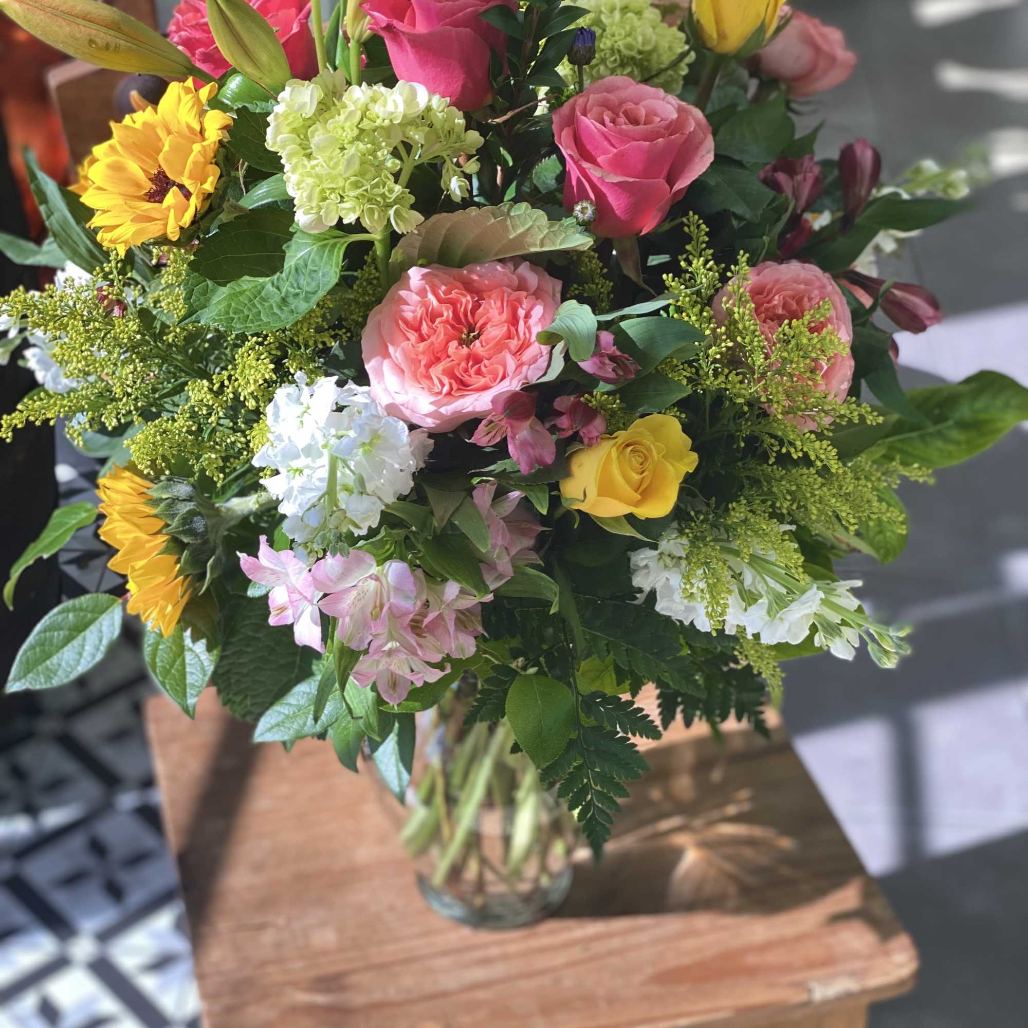 Mixed bouquet of roses, sunflowers, lilies, and hydrangea in a glass vase
