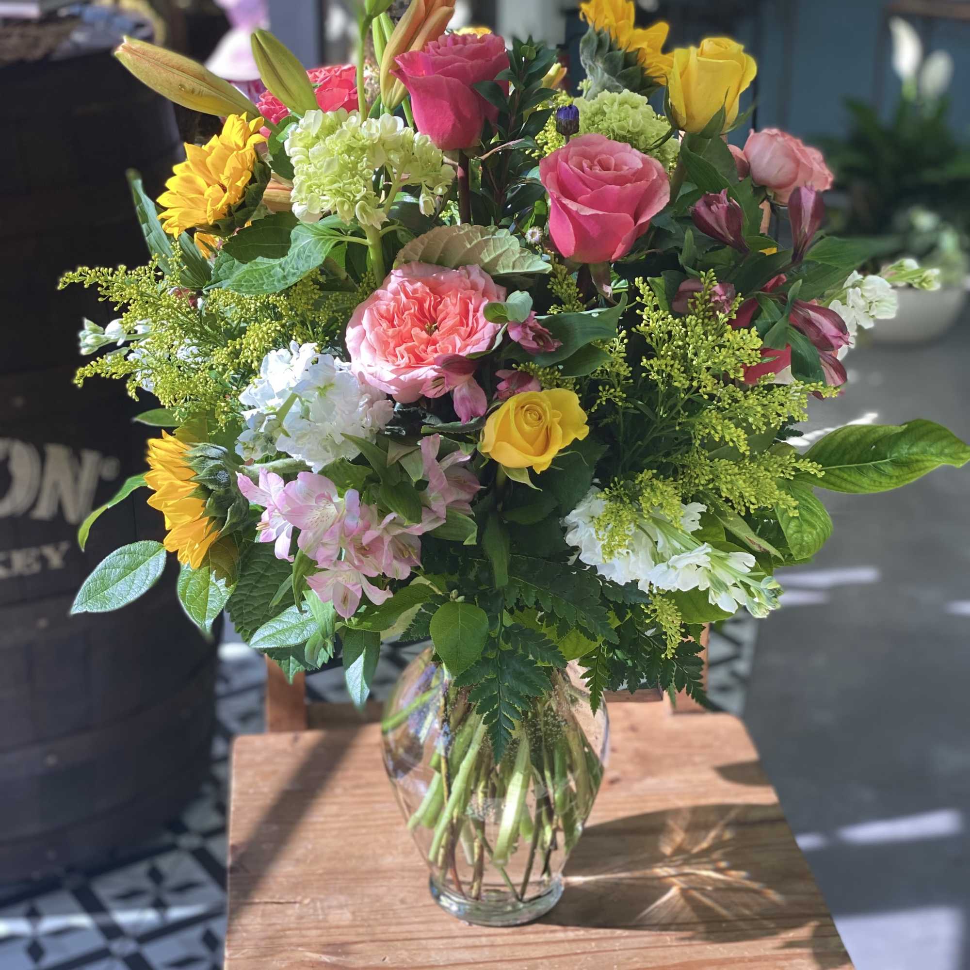 Mixed bouquet of roses, lilies, sunflowers, and hydrangeas in a glass vase