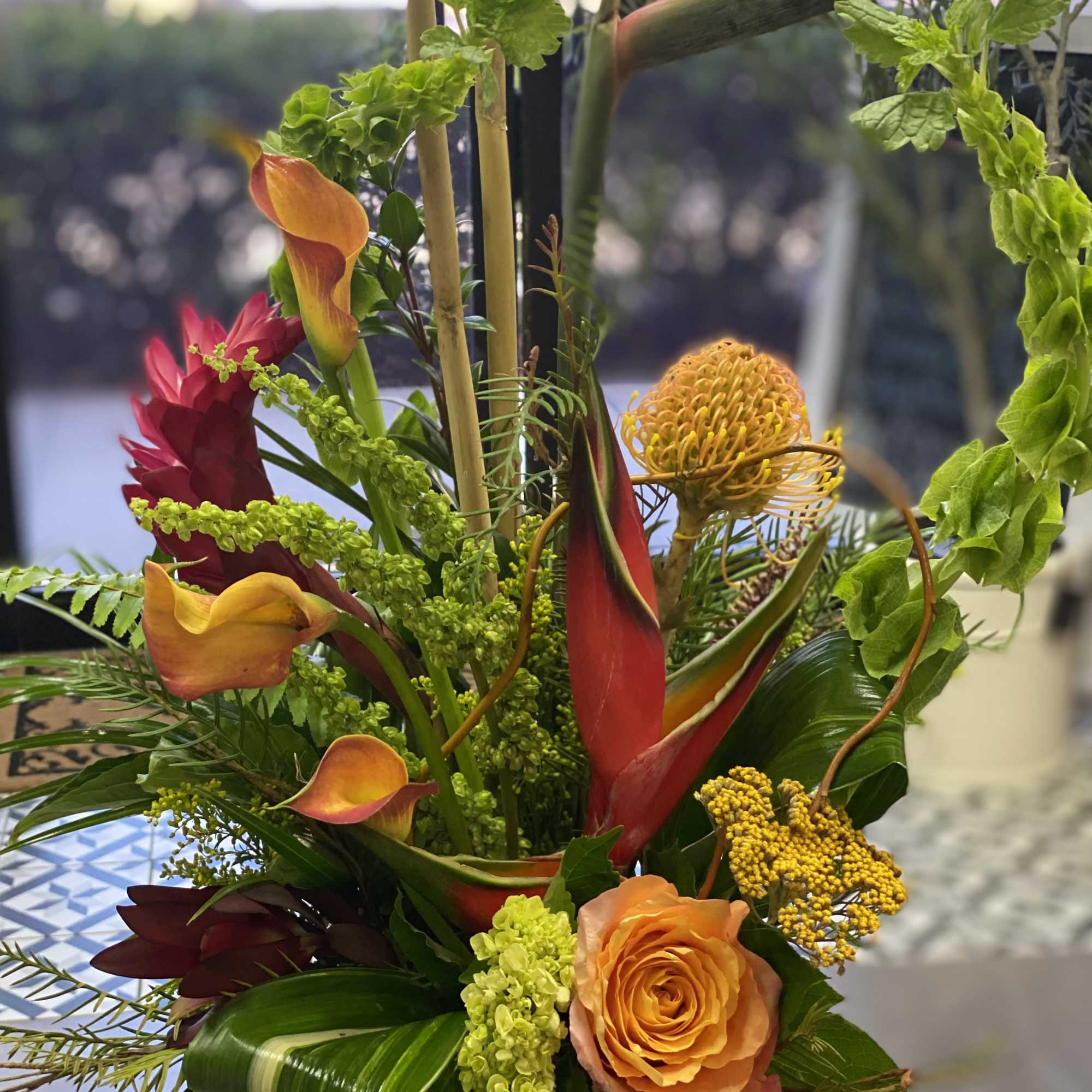 Tropical floral arrangement with orange roses and calla lilies in a glass vase