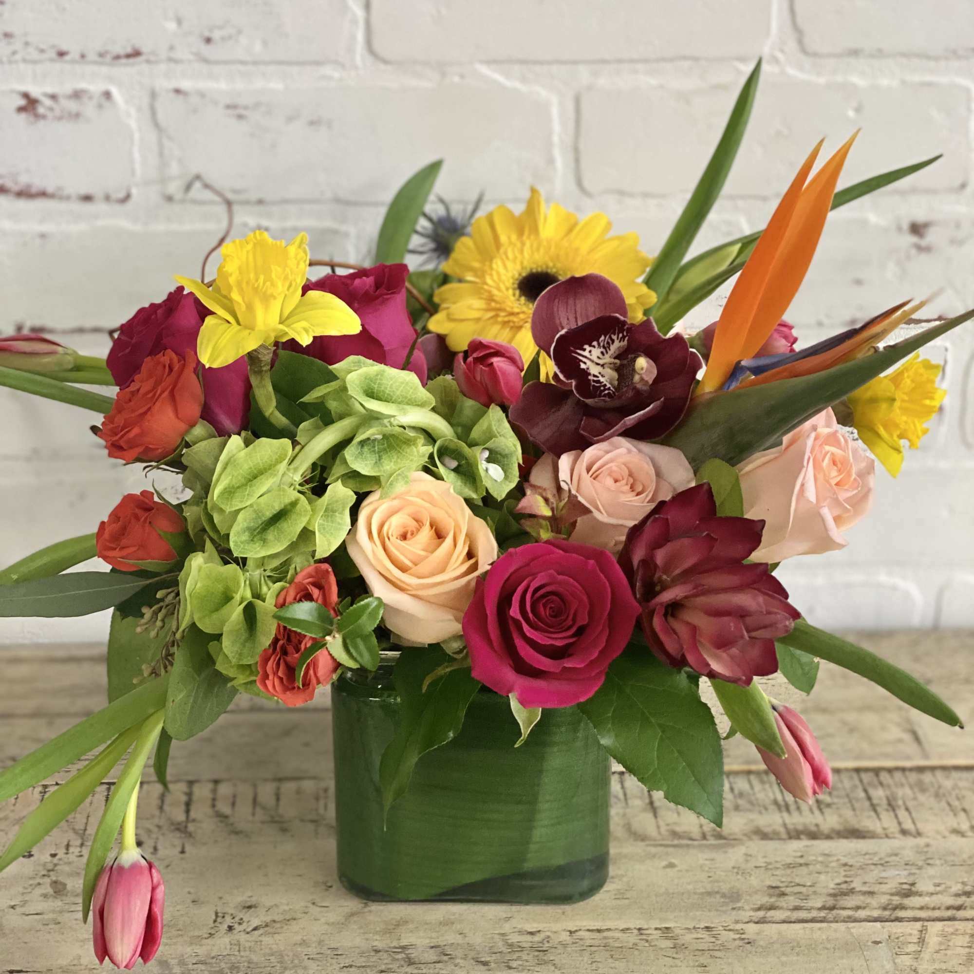 Mixed bouquet of roses, orchids, and bright tropical flowers in a green vase
