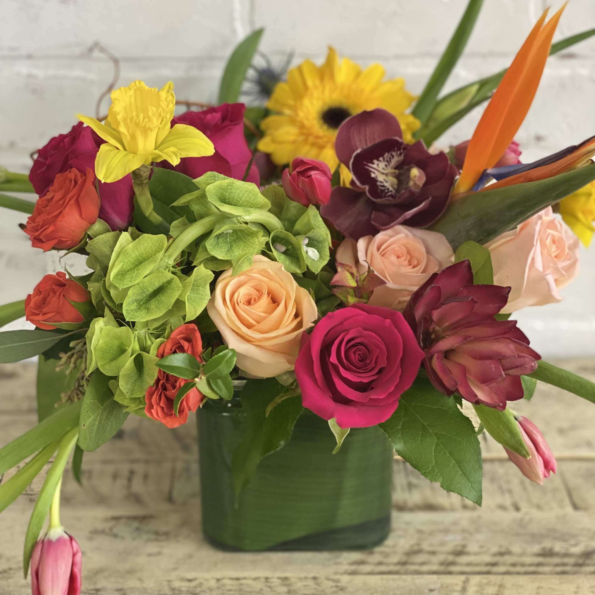 Mixed bouquet in a green vase with roses and bright tropical blooms