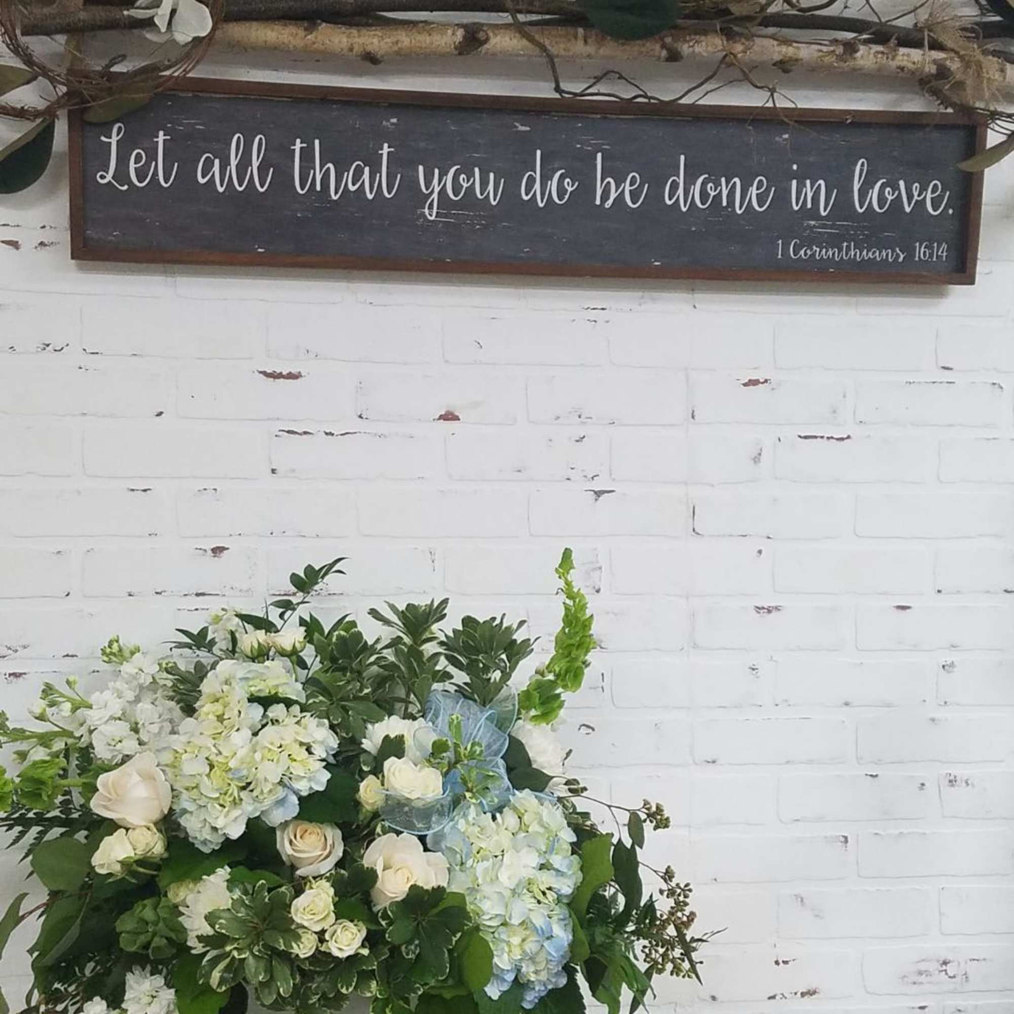 White floral arrangement in a white bucket beneath a rustic wall sign