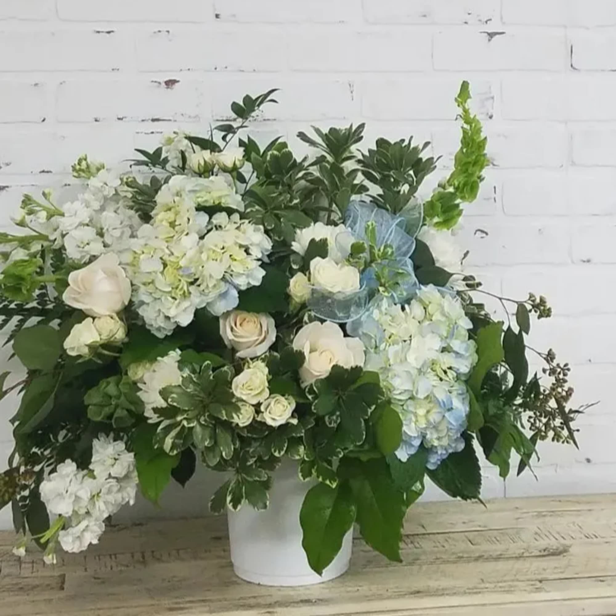 White and pale blue floral arrangement in a white vase