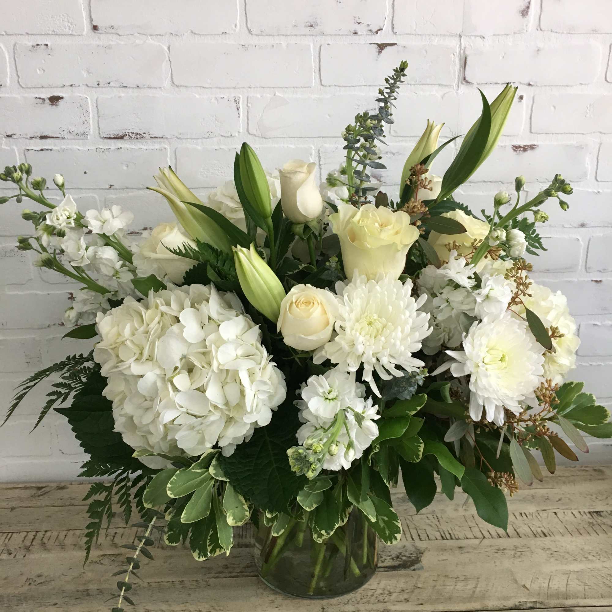 White hydrangeas, roses, lilies, and mums arranged in a clear glass vase
